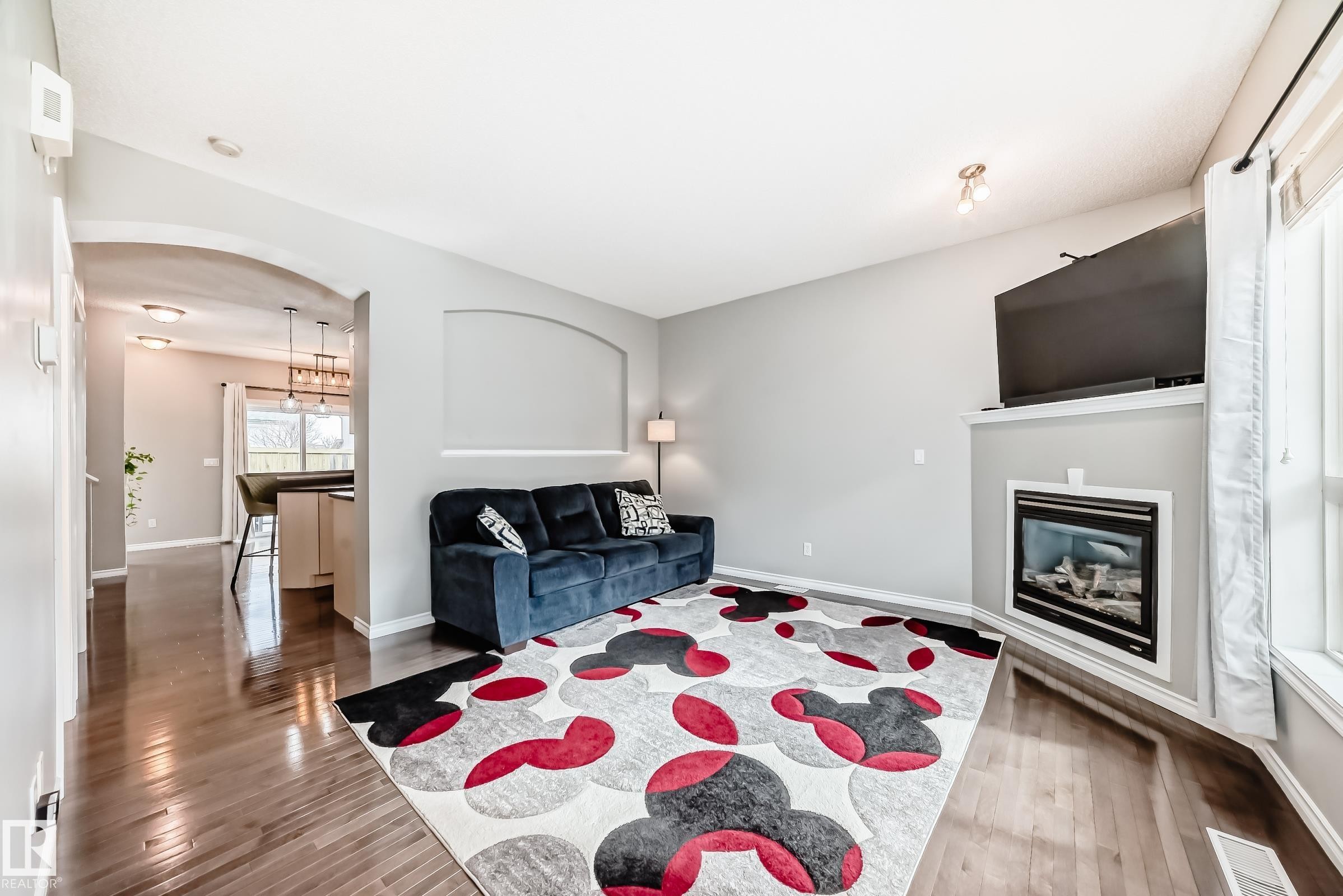 Spacious living area featuring wood-finish flooring, a built-in electric fireplace with a mantel, and an arched hallway entry - 105 13825 155 Avenue, Edmonton, AB - Indoor Photo Showing Living Room With Fireplace