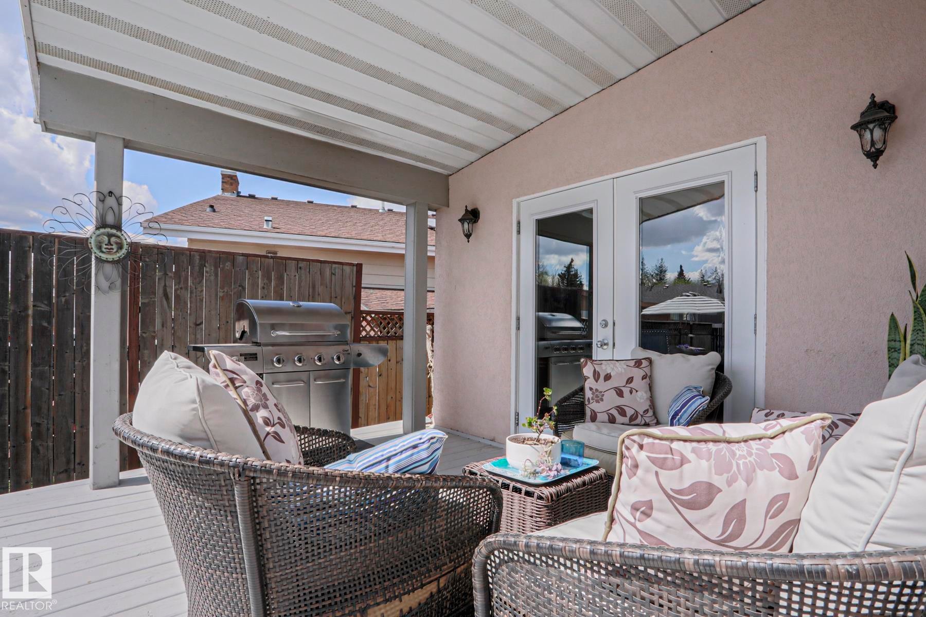 Covered outdoor deck with white painted wood-finish flooring, featuring a stucco exterior wall and white-framed double French doors - 1214 85 Street Nw, Edmonton, AB - Outdoor With Deck Patio Veranda With Exterior