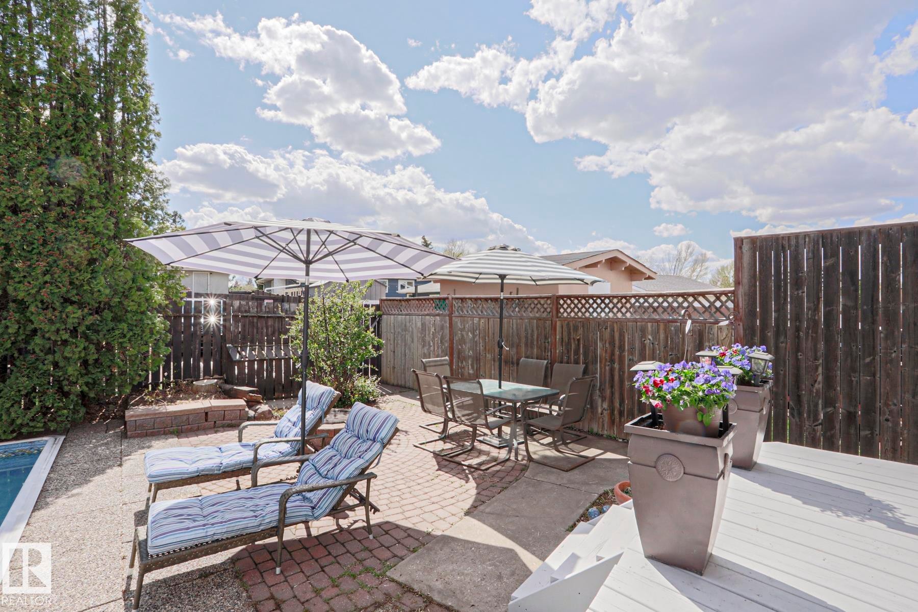 Outdoor living space featuring a white painted deck, brick paver patio, and a gravel area surrounding a pool - 1214 85 Street Nw, Edmonton, AB - Outdoor With Deck Patio Veranda