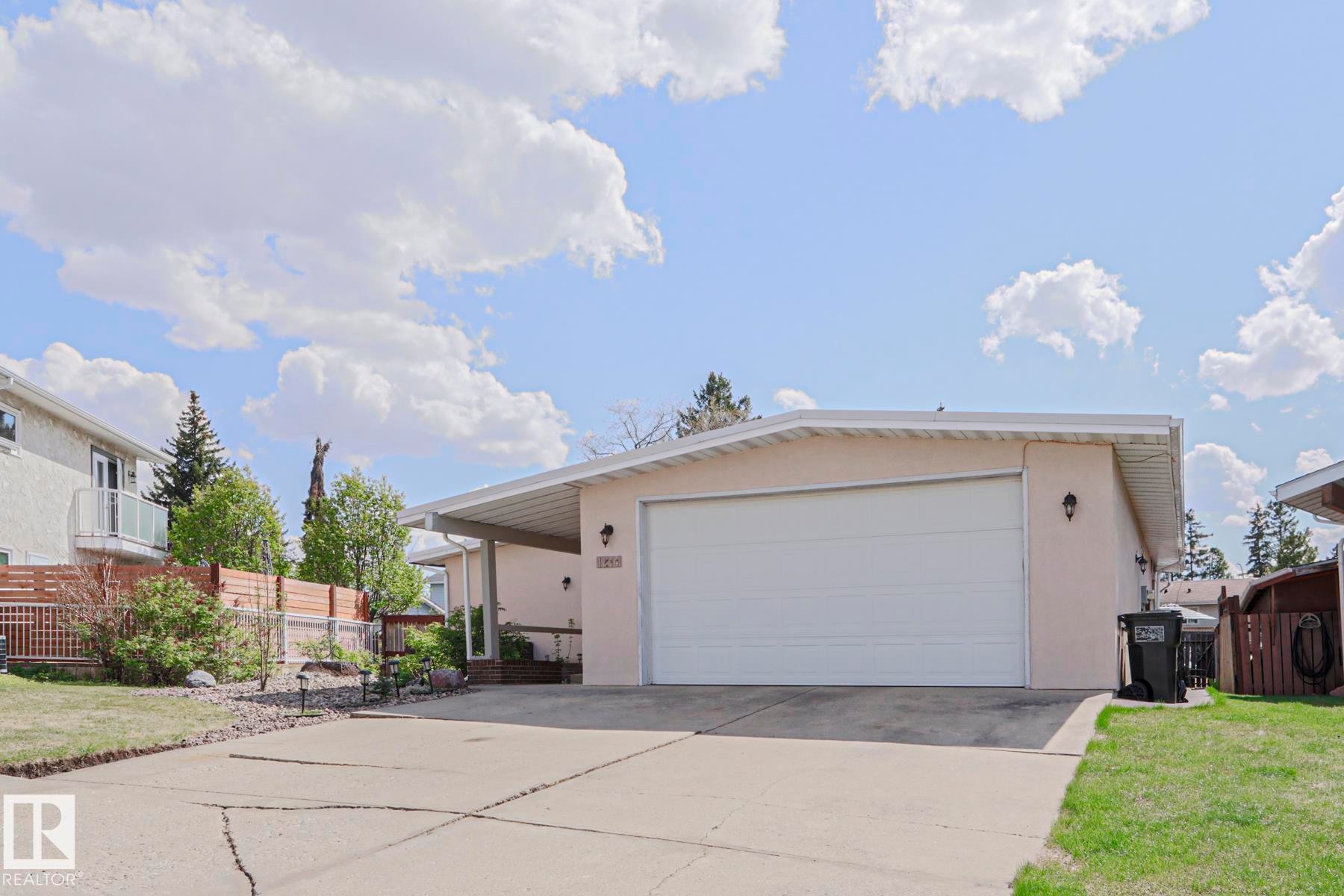 Contemporary stucco exterior with a white garage door, featuring an attached carport - 1214 85 Street Nw, Edmonton, AB - Outdoor