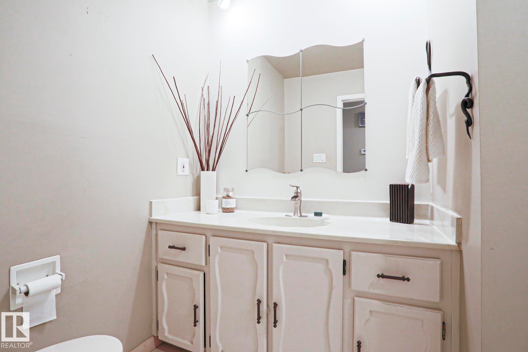Bathroom vanity featuring a single basin sink set in a light-toned countertop, white cabinetry with dark hardware, and a decorative wall mirror - 1214 85 Street Nw, Edmonton, AB - Indoor Photo Showing Bathroom
