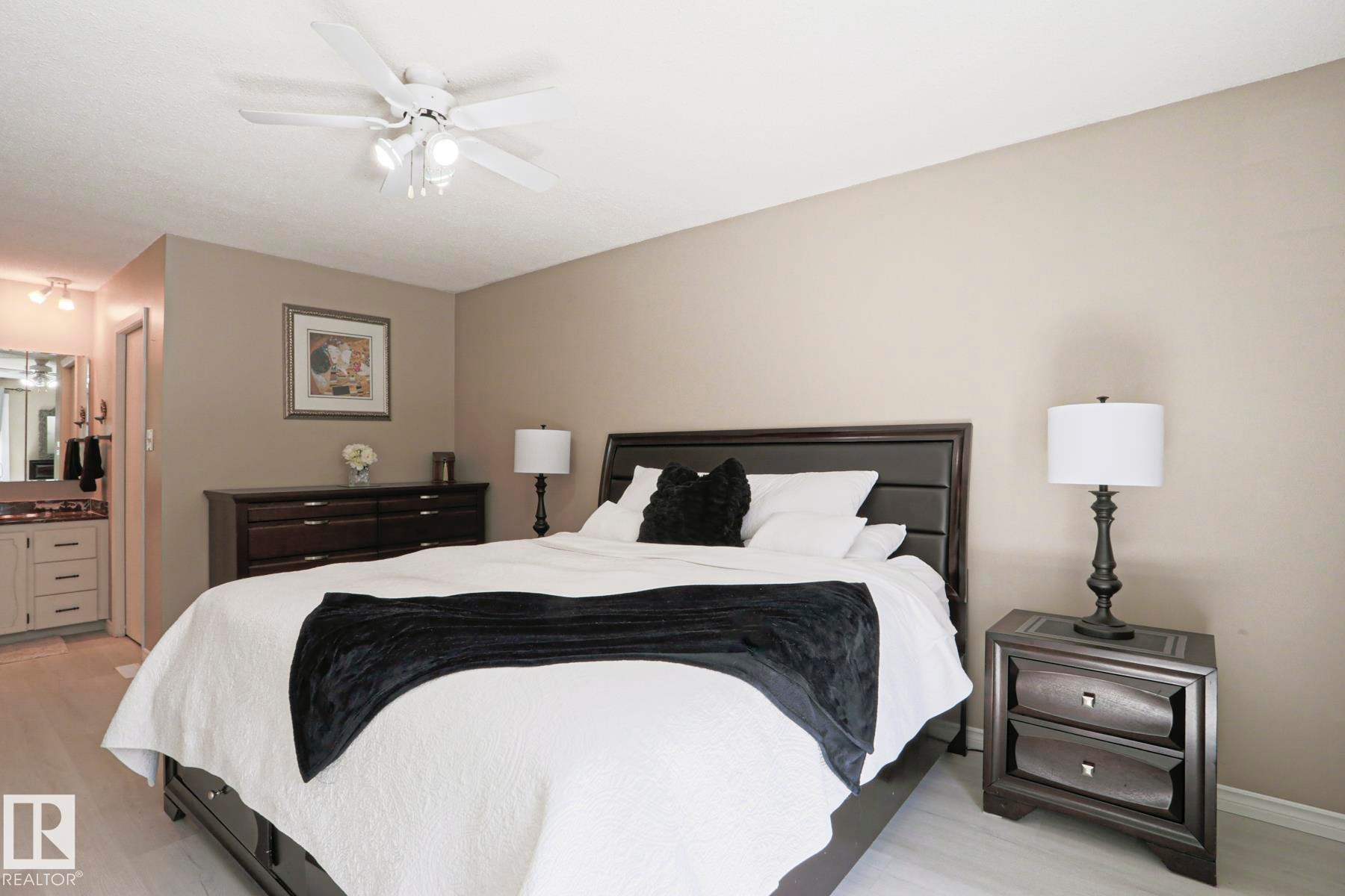 Bedroom featuring a white ceiling fan with integrated lighting, wood-finish flooring, and a vanity area with a built-in sink and mirror - 1214 85 Street Nw, Edmonton, AB - Indoor Photo Showing Bedroom