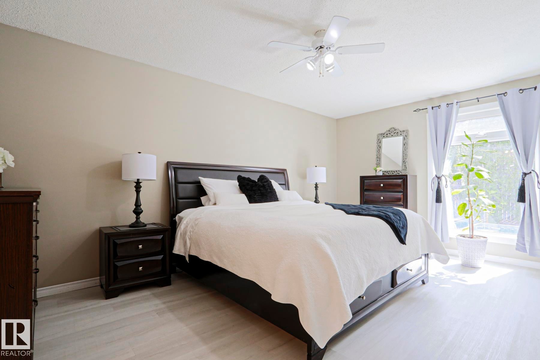 Bedroom featuring light wood-finish flooring, a large window with drapes, a ceiling fan with integrated lighting, and neutral wall tones - 1214 85 Street Nw, Edmonton, AB - Indoor Photo Showing Bedroom