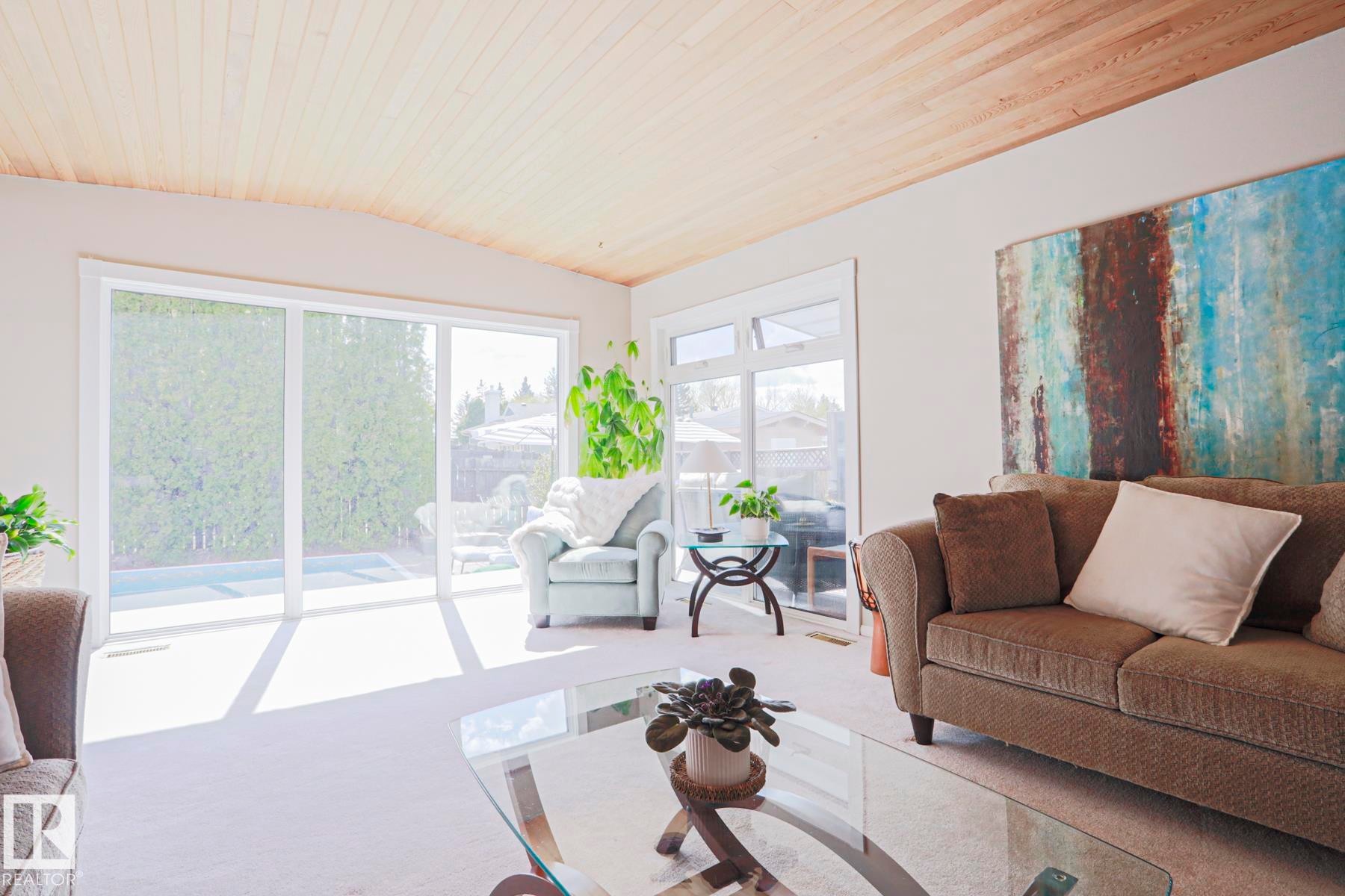 Spacious living area featuring a light-colored wood-paneled ceiling, large sliding glass doors, multiple windows, and light-toned carpeting - 1214 85 Street Nw, Edmonton, AB - Indoor Photo Showing Living Room