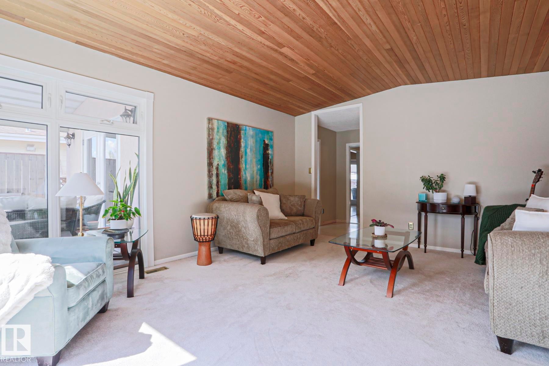 Living area featuring a wood-panel ceiling, light neutral wall paint, and light-colored carpeting - 1214 85 Street Nw, Edmonton, AB - Indoor