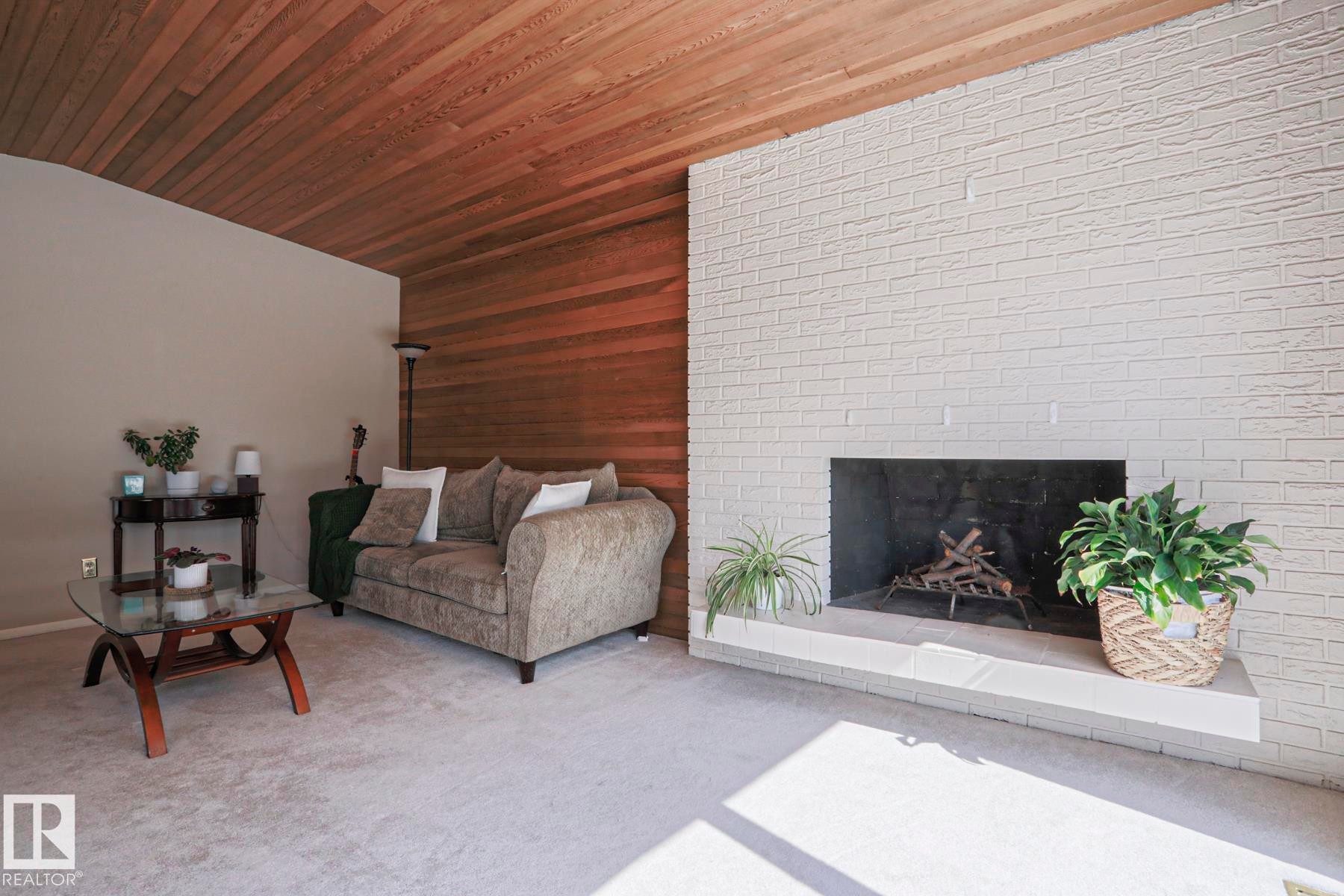 Living area featuring a painted brick fireplace with a stone hearth, a wood-paneled accent wall, and a sloped wood-finish ceiling - 1214 85 Street Nw, Edmonton, AB - Indoor Photo Showing Living Room