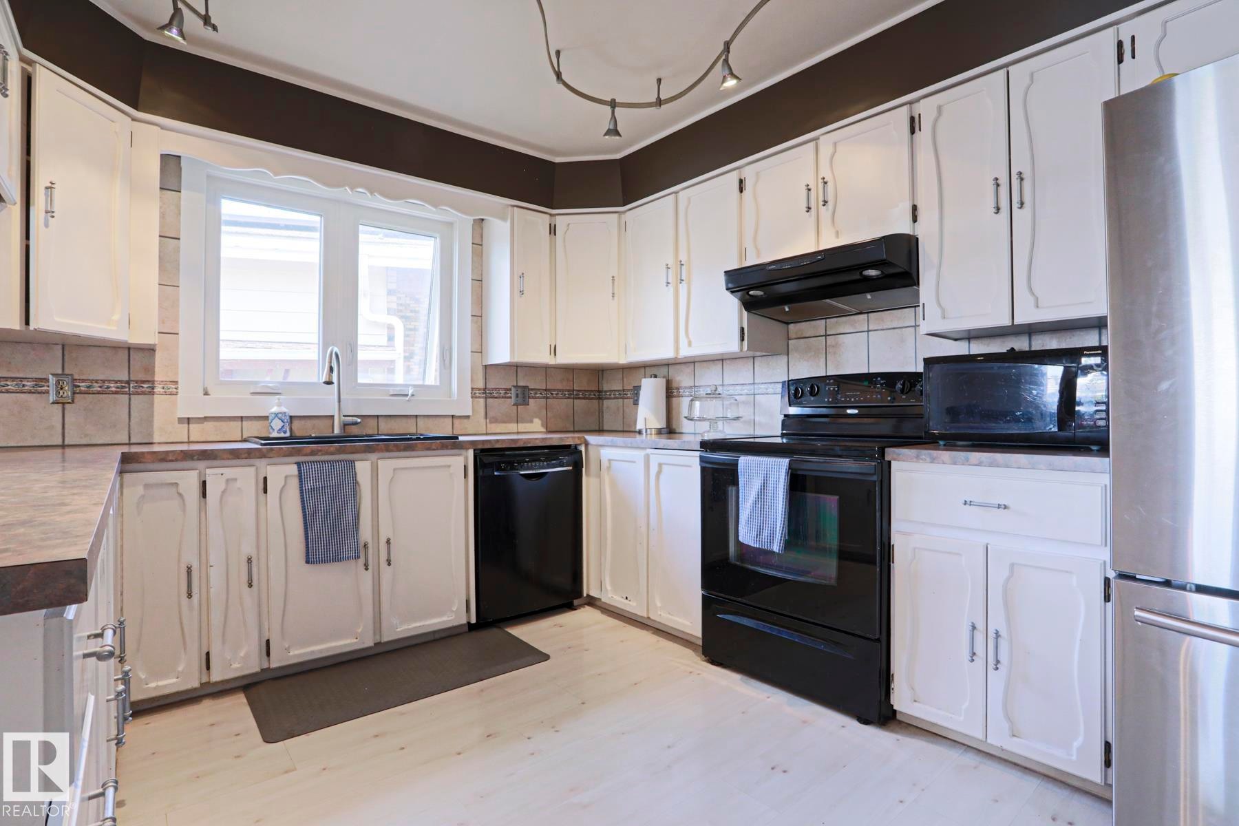 Kitchen featuring white cabinetry with dark hardware, dark countertops, and a tiled backsplash - 1214 85 Street Nw, Edmonton, AB - Indoor Photo Showing Kitchen