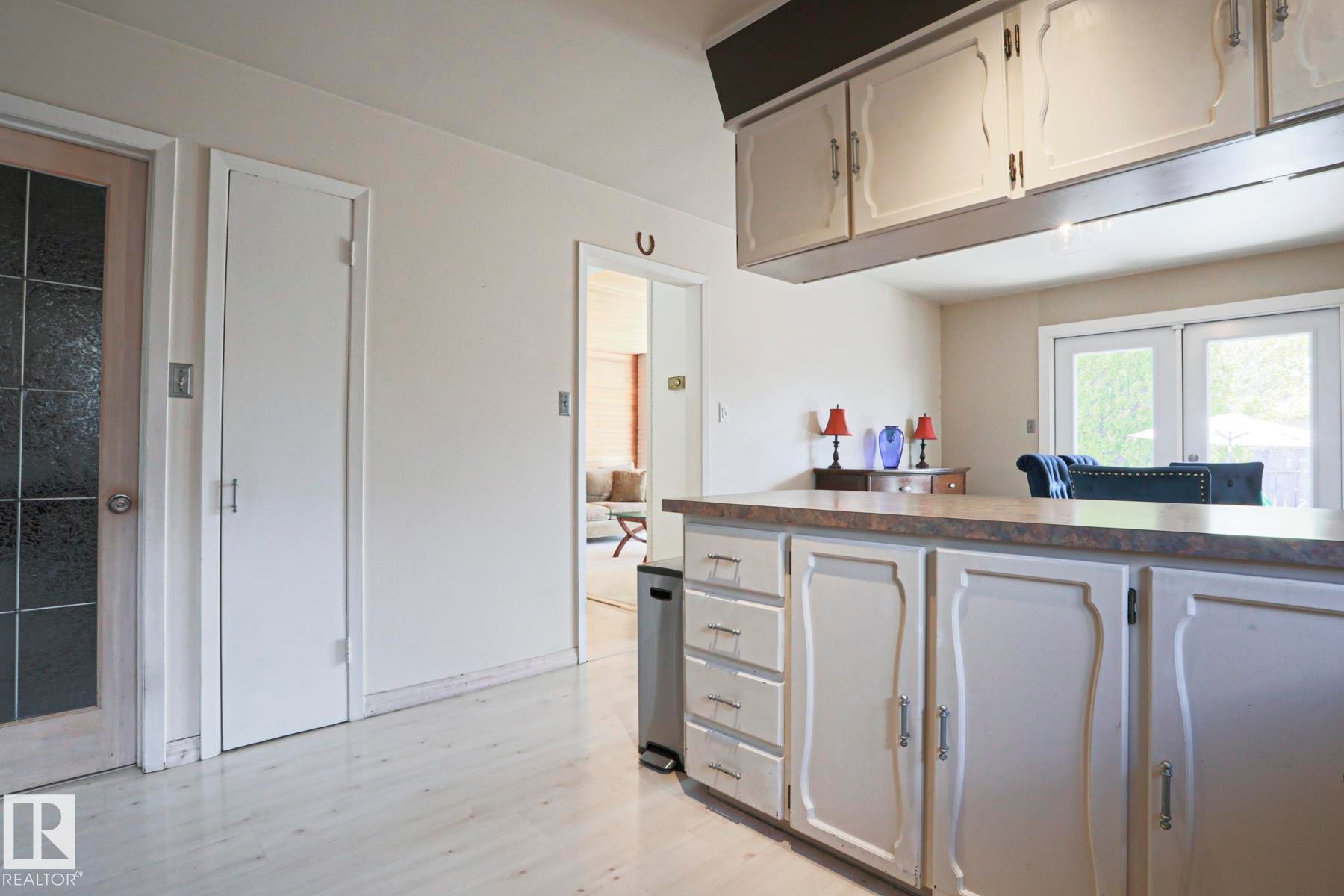 Kitchen cabinetry featuring decorative paneling, an extended countertop, and upper storage with integrated lighting - 1214 85 Street Nw, Edmonton, AB - Indoor