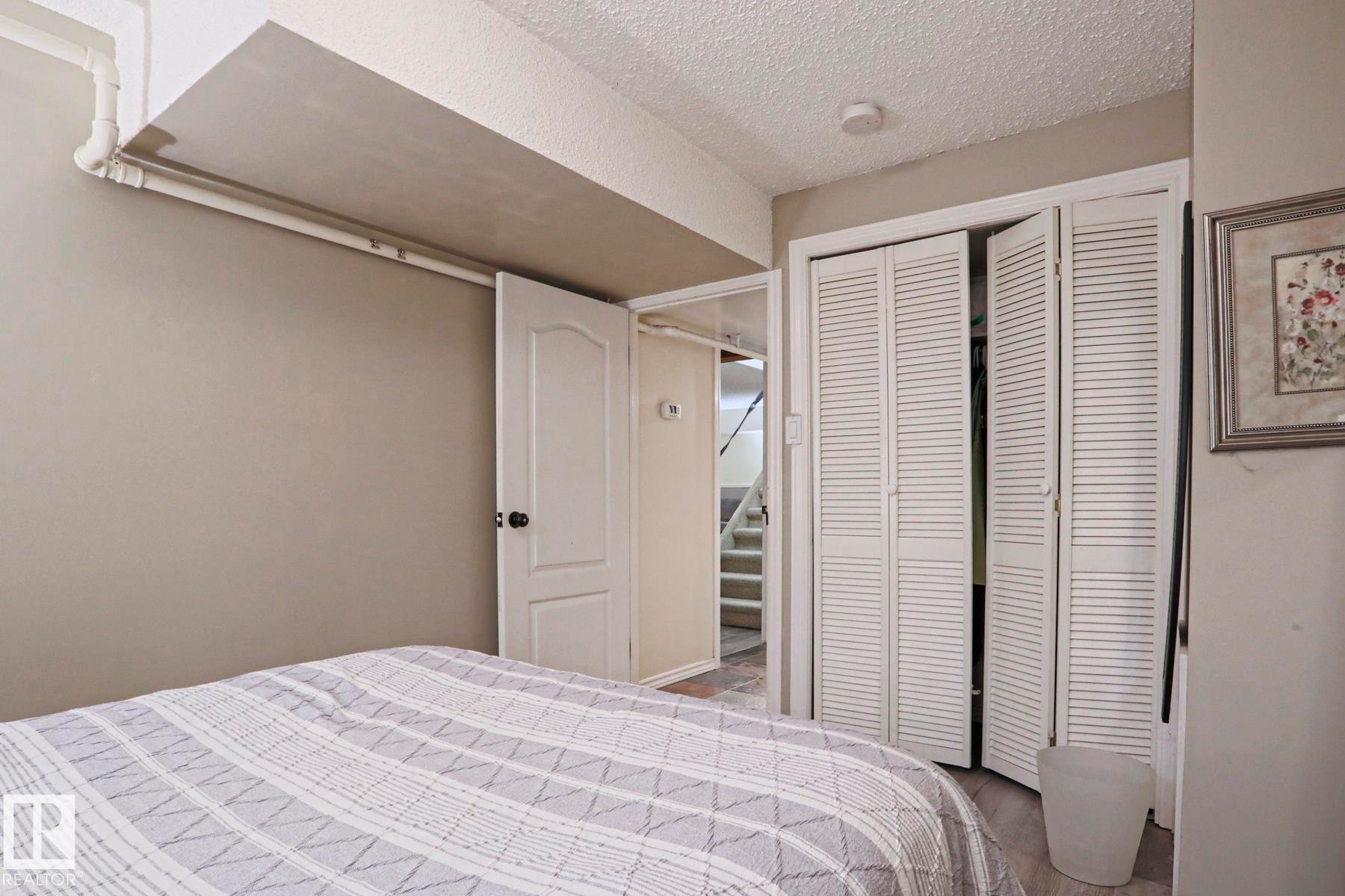 Interior room featuring light gray walls, wood-finish flooring, a white paneled door, and white louvered bifold closet doors - 1214 85 Street Nw, Edmonton, AB - Indoor Photo Showing Bedroom