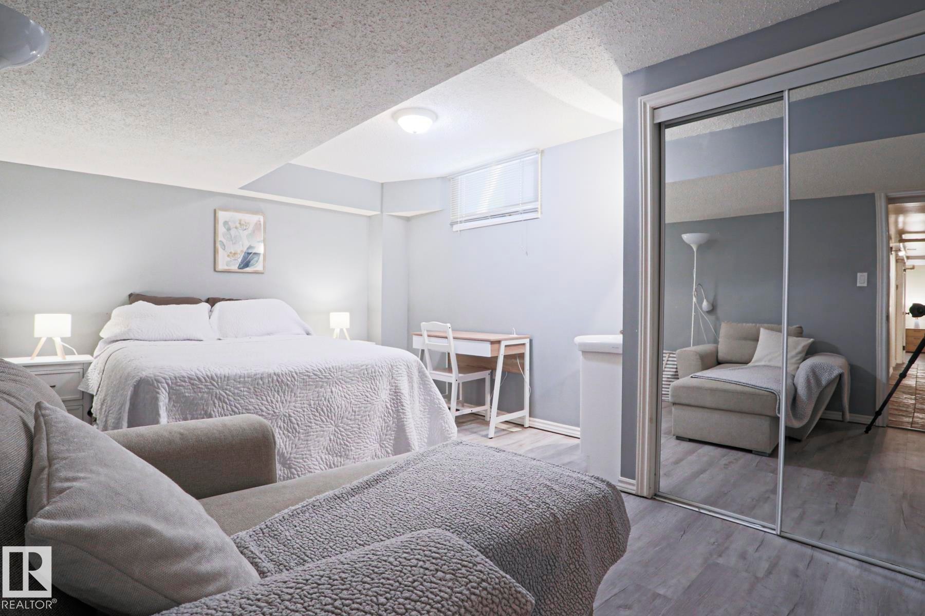 Bedroom featuring light gray walls, wood-finish flooring, a built-in window, and mirrored closet doors - 1214 85 Street Nw, Edmonton, AB - Indoor Photo Showing Bedroom