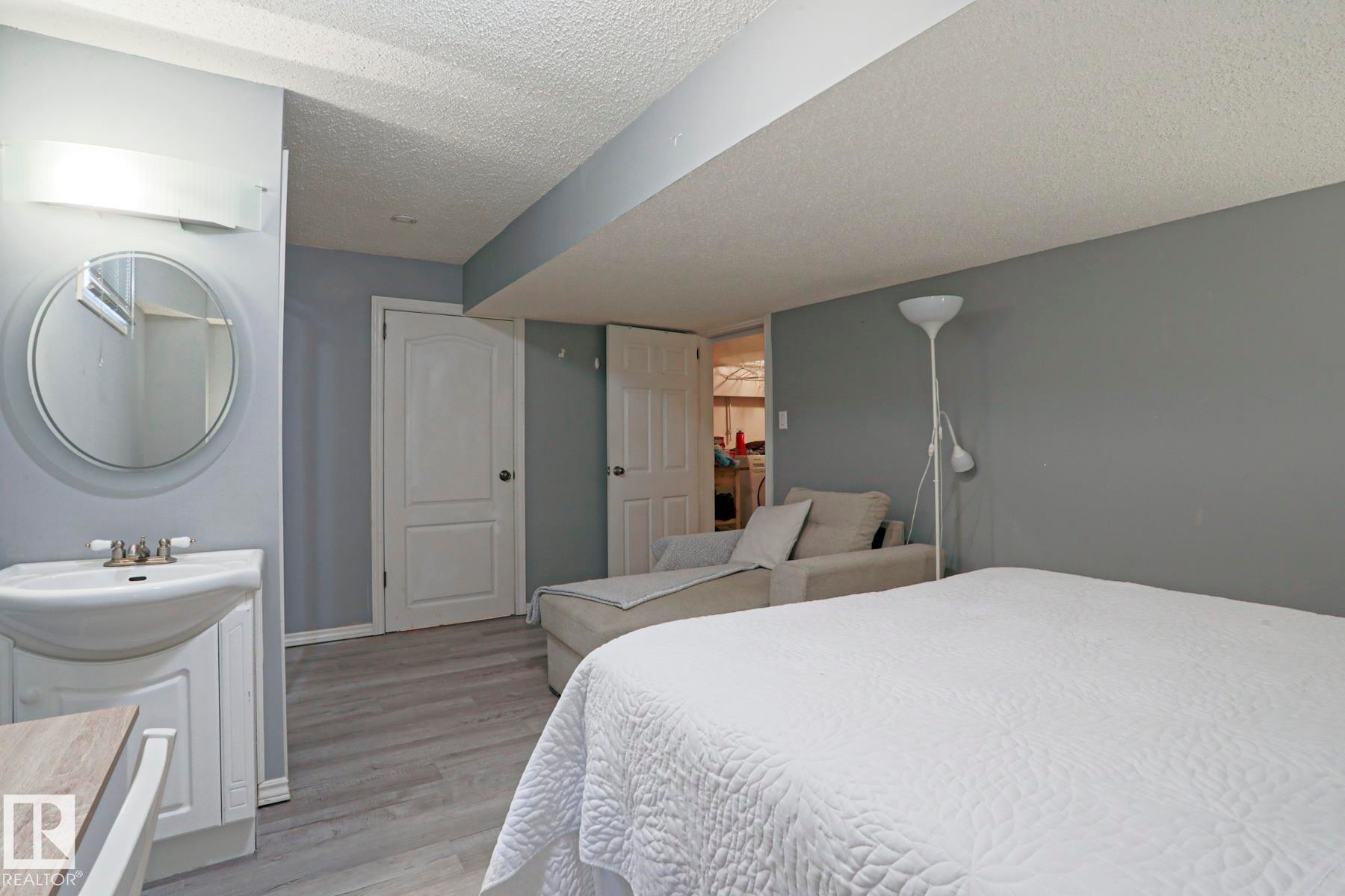 Pedestal sink vanity with a circular mirror and overhead bar lighting - 1214 85 Street Nw, Edmonton, AB - Indoor Photo Showing Bedroom