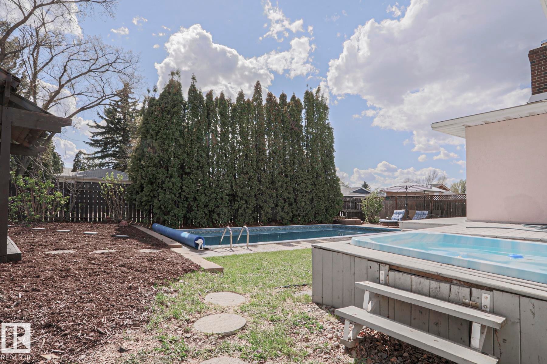 Expansive backyard featuring an in-ground swimming pool, an elevated hot tub with wooden surround and steps, a privacy hedge of tall evergreens, a wooden fence, and a gazebo structure - 1214 85 Street Nw, Edmonton, AB - Outdoor