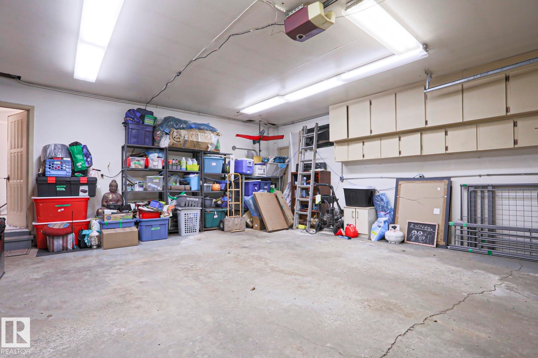 Spacious garage featuring a concrete floor, built-in overhead cabinetry, fluorescent lighting, and a garage door opener - 1214 85 Street Nw, Edmonton, AB - Indoor Photo Showing Garage
