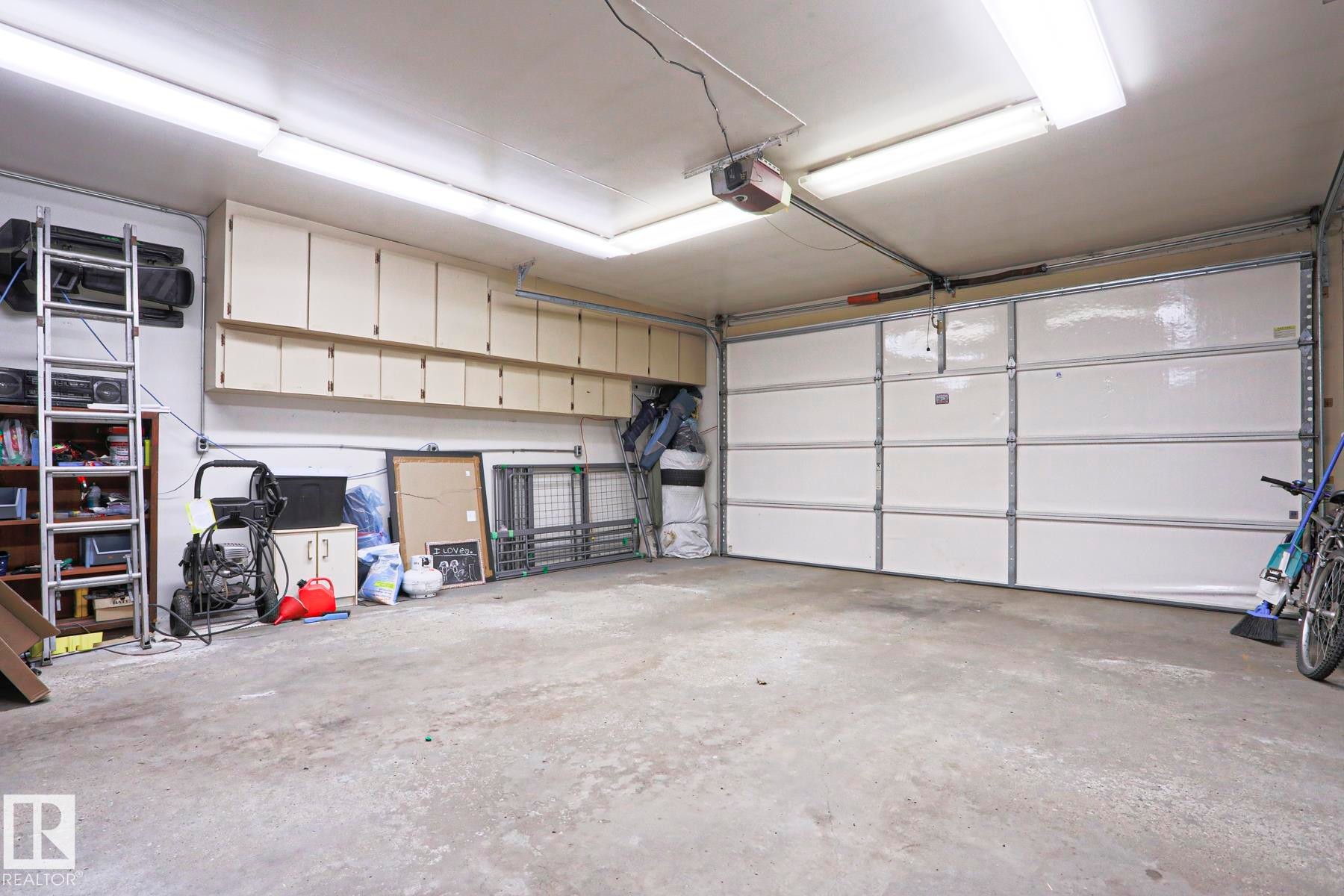 Attached garage featuring a sectional overhead door, overhead fluorescent lighting, and extensive wall-mounted cabinetry - 1214 85 Street Nw, Edmonton, AB - Indoor Photo Showing Garage
