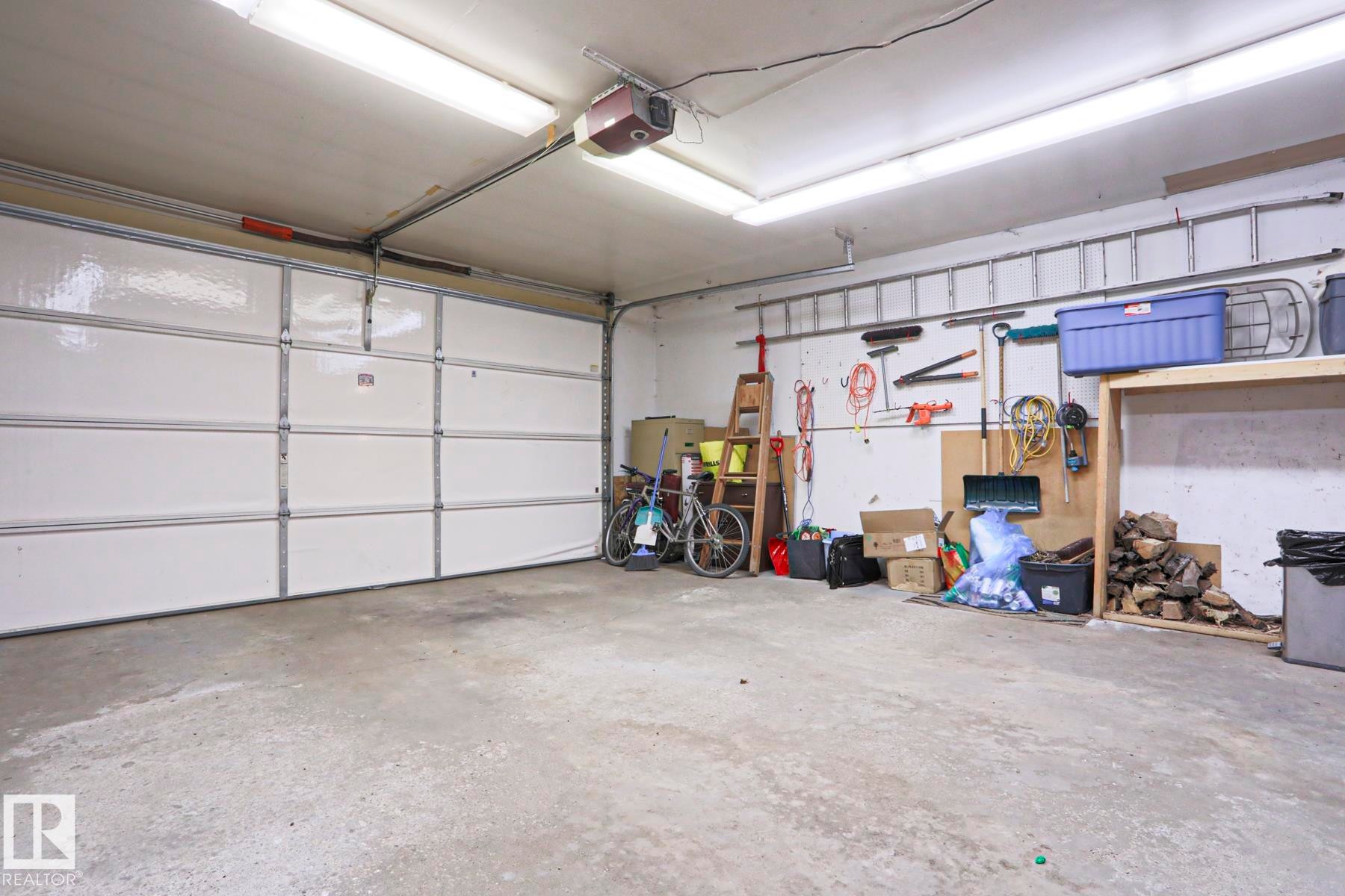 Spacious garage featuring a white panel garage door, concrete flooring, and ceiling-mounted strip lighting - 1214 85 Street Nw, Edmonton, AB - Indoor Photo Showing Garage