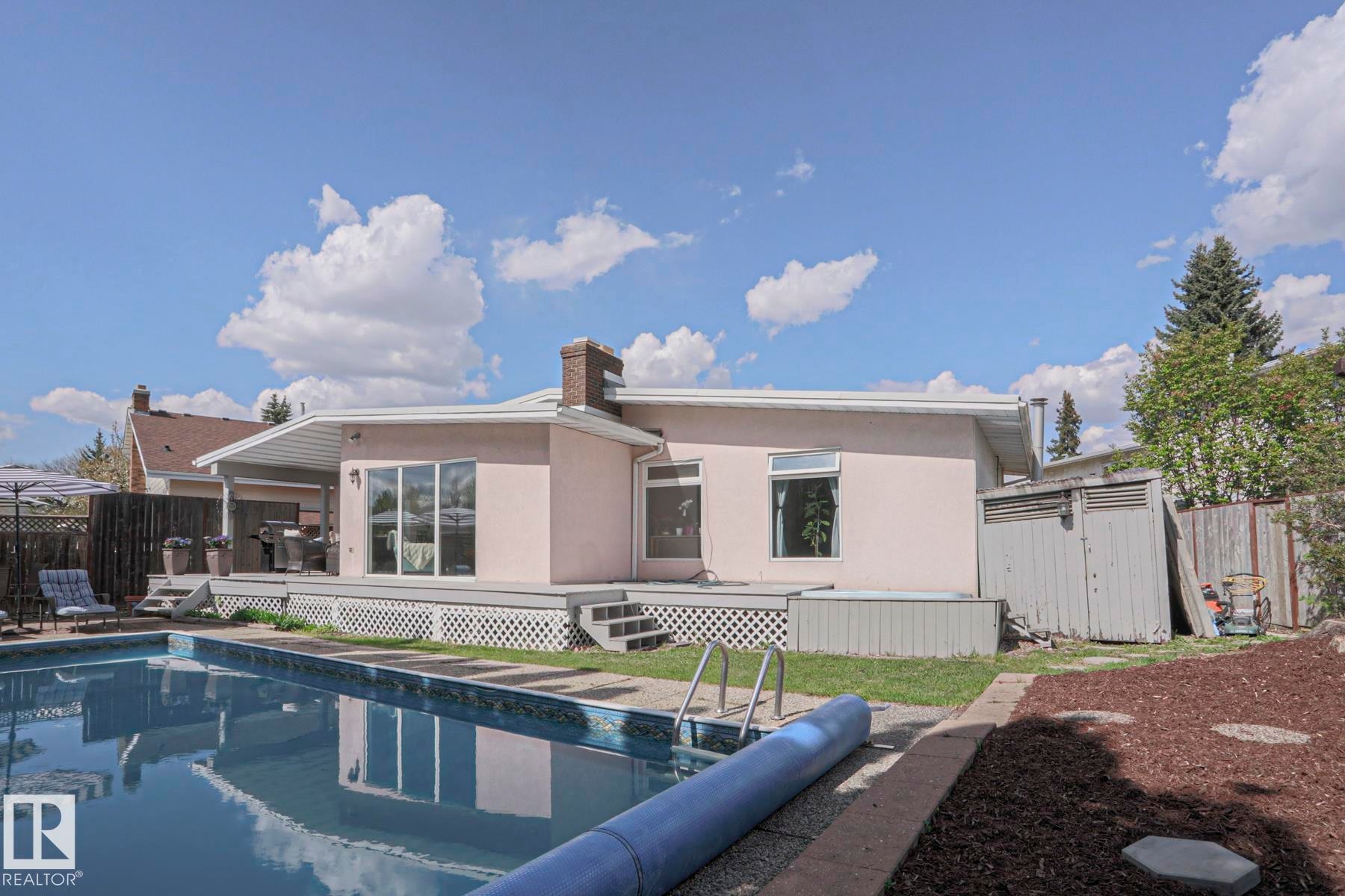 Expansive backyard featuring a rectangular swimming pool with integrated steps, a multi-level wood deck, a covered patio area, and a stucco exterior - 1214 85 Street Nw, Edmonton, AB - Outdoor With In Ground Pool