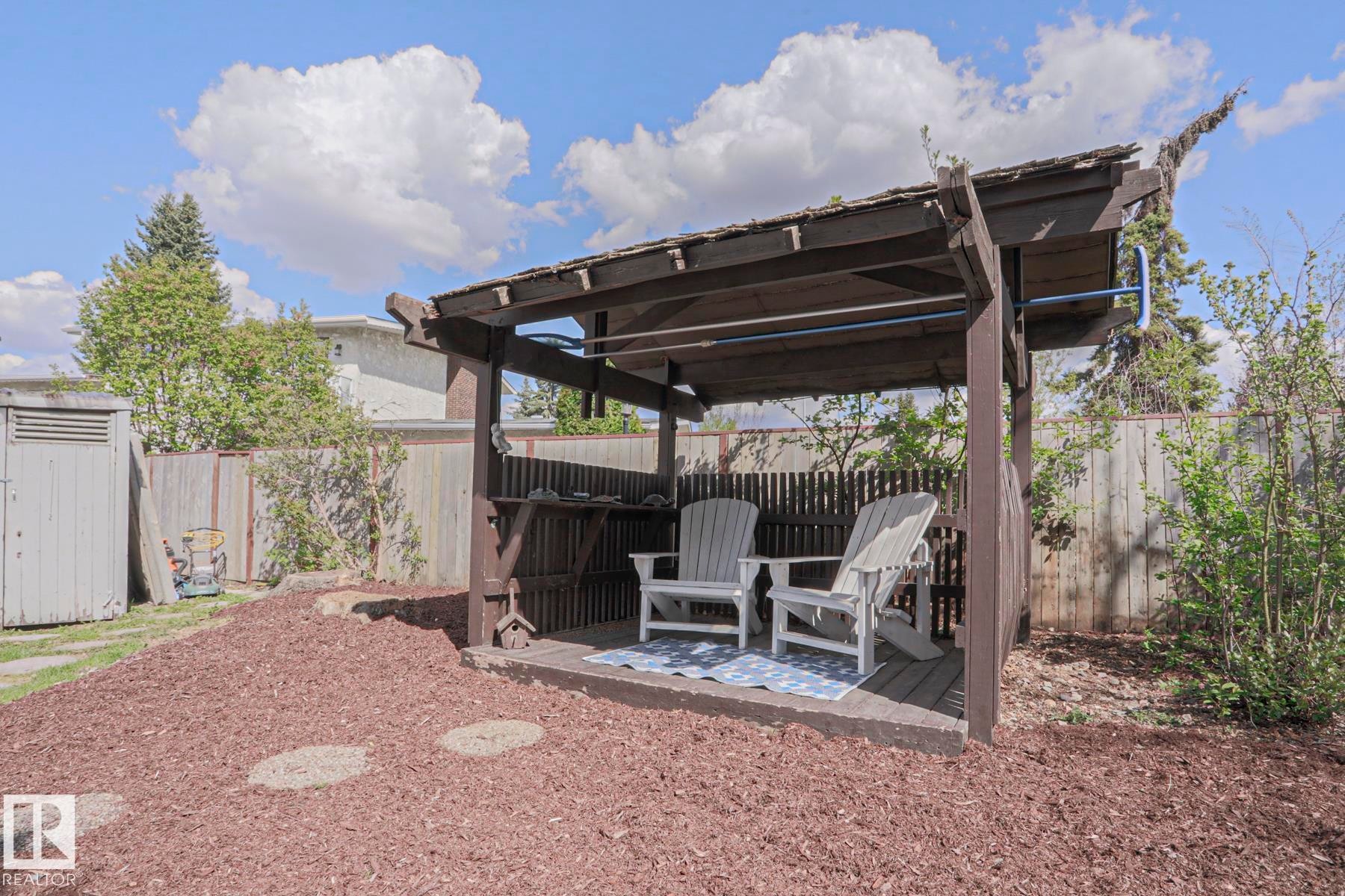 Outdoor wooden pergola with a built-in shelf, elevated deck flooring, and a mulched ground cover - 1214 85 Street Nw, Edmonton, AB - Outdoor With Deck Patio Veranda