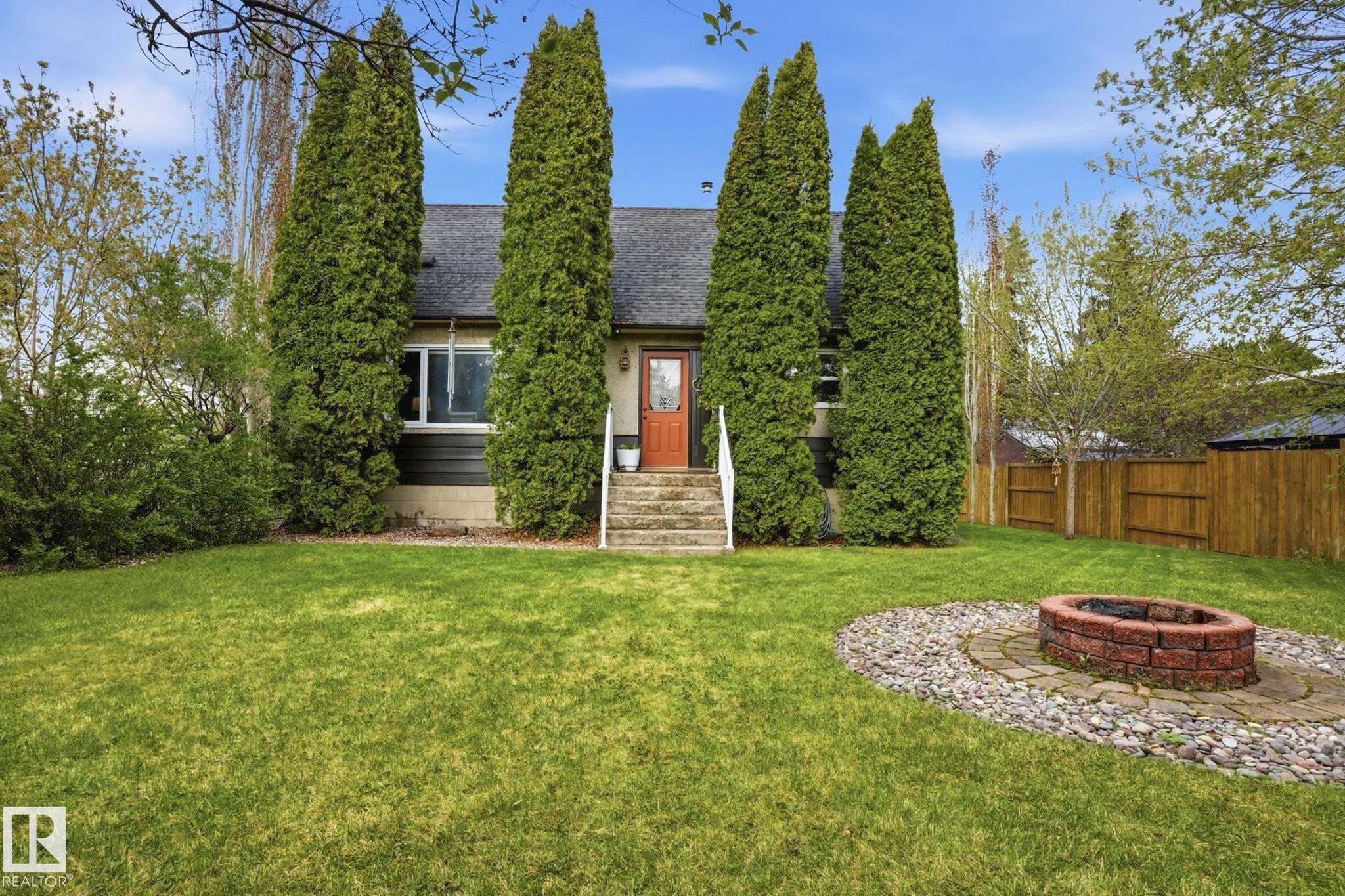 Expansive lawn area featuring a brick fire pit with a stone and paver surround - 4 Langley Dr, Fort Saskatchewan, AB - Outdoor