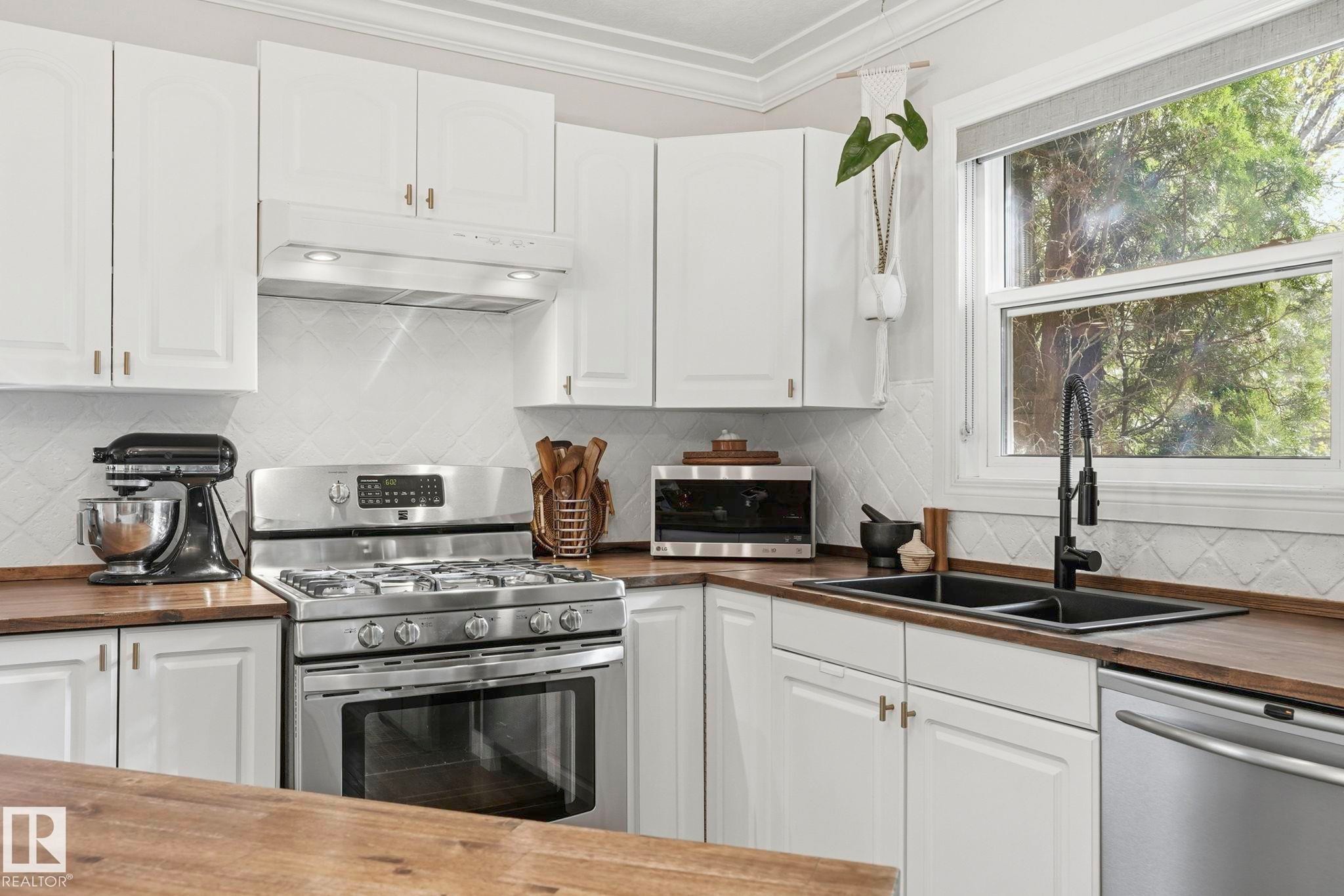 Kitchen featuring white cabinetry, wood-finish countertops, stainless steel appliances, a white tile backsplash, and a double basin sink with a matte black faucet - 4 Langley Dr, Fort Saskatchewan, AB - Indoor Photo Showing Kitchen With Double Sink