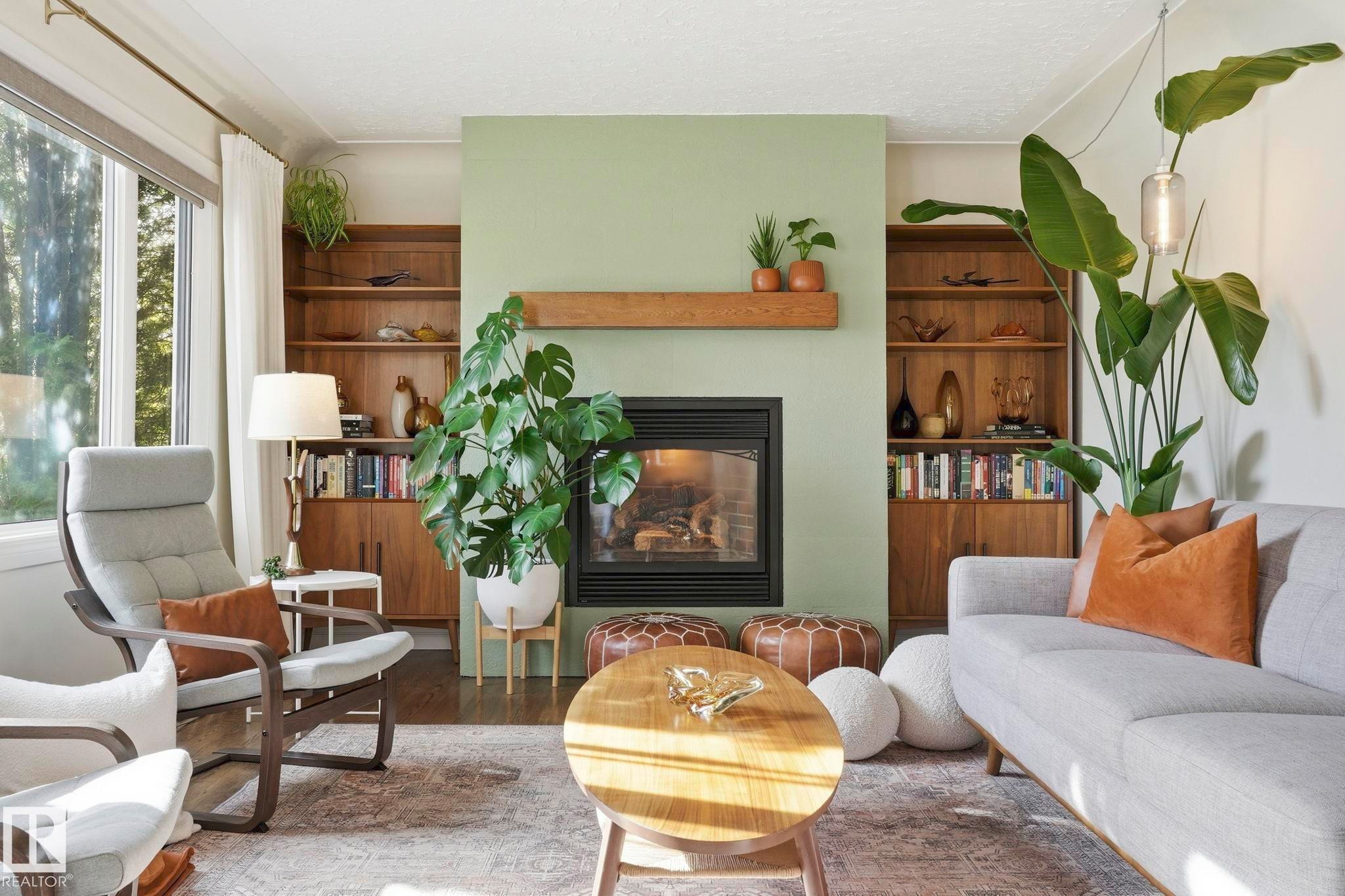 Living area featuring a fireplace with a wood mantle and built-in shelving, large windows, and wood-finish flooring - 4 Langley Dr, Fort Saskatchewan, AB - Indoor Photo Showing Living Room With Fireplace