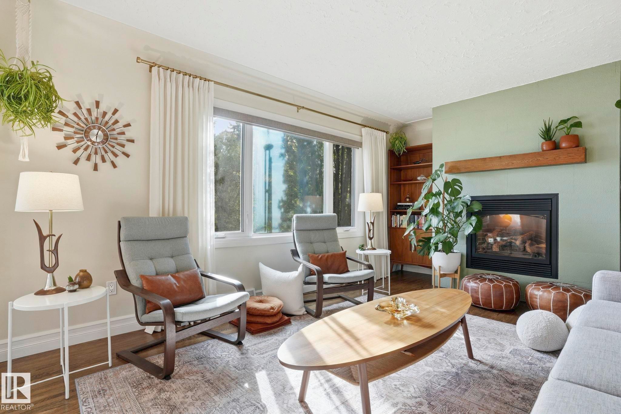 Living area featuring a fireplace with a wood mantel, built-in shelving, large window with drapes, and wood-finish flooring partially covered by an area rug - 4 Langley Dr, Fort Saskatchewan, AB - Indoor Photo Showing Living Room With Fireplace