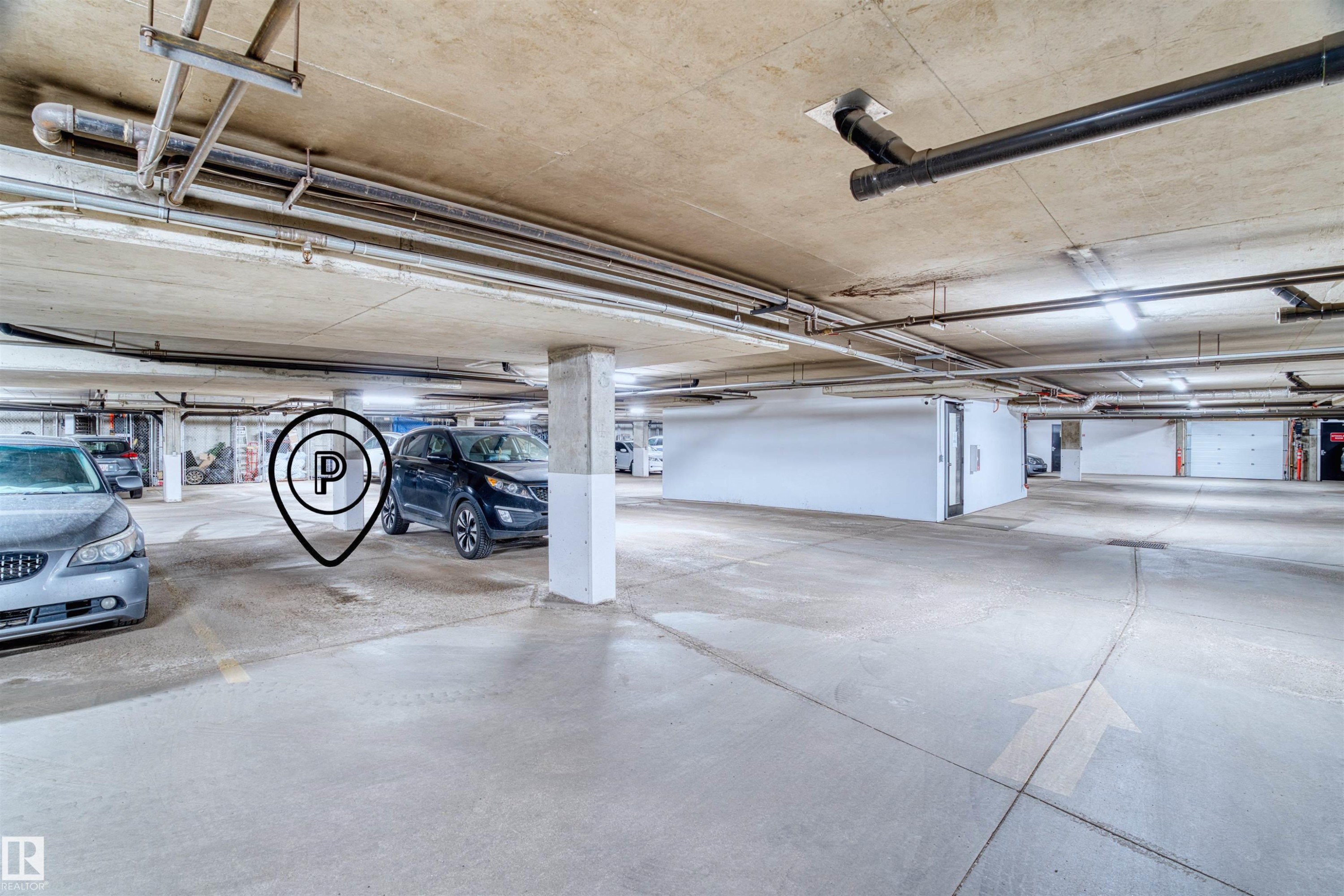 Covered parking garage featuring concrete flooring, exposed overhead piping, column supports, and fluorescent lighting - 205 10939 82 Avenue, Edmonton, AB - Indoor Photo Showing Garage