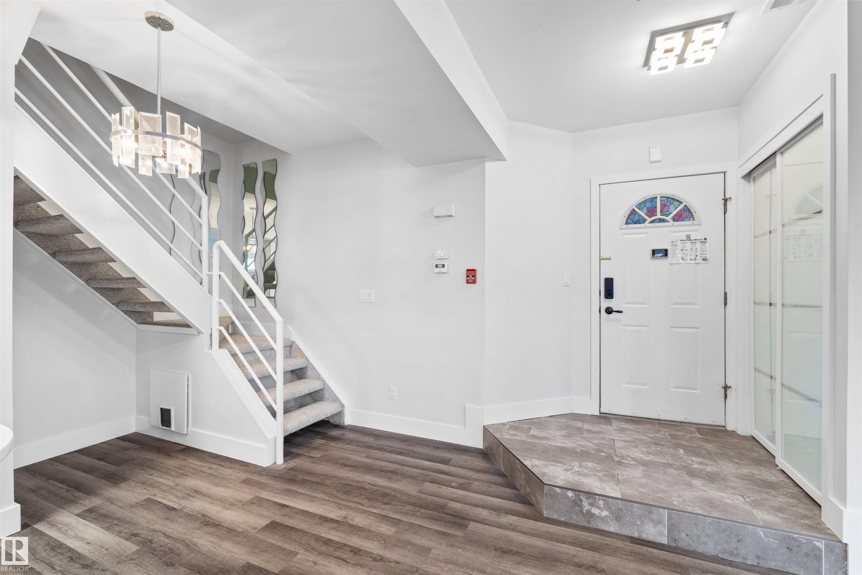 Entryway featuring wood-finish flooring, a contemporary chandelier, a white staircase with carpeted treads, and a tiled landing - 205 10939 82 Avenue, Edmonton, AB - Indoor Photo Showing Other Room