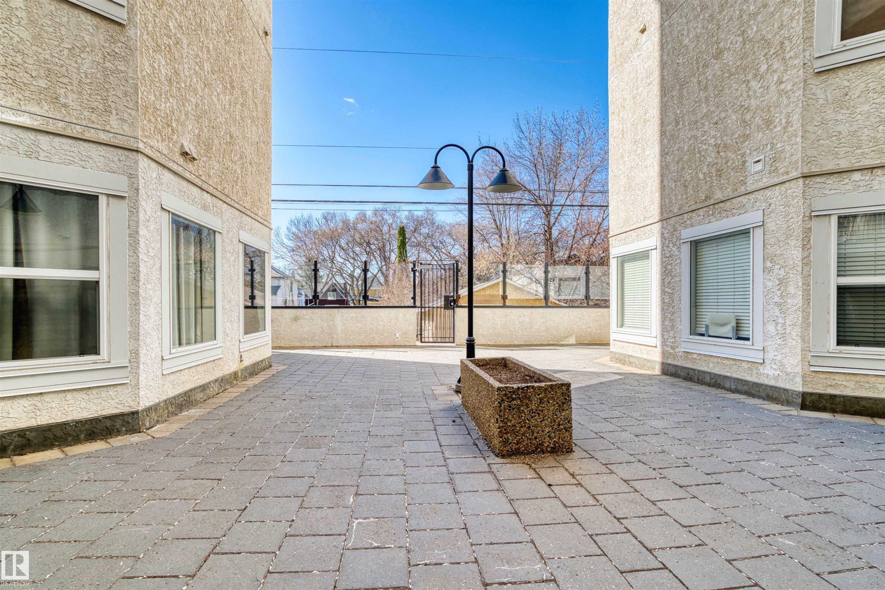 Paved courtyard featuring textured stucco exterior walls and multiple windows - 205 10939 82 Avenue, Edmonton, AB - Outdoor With Exterior