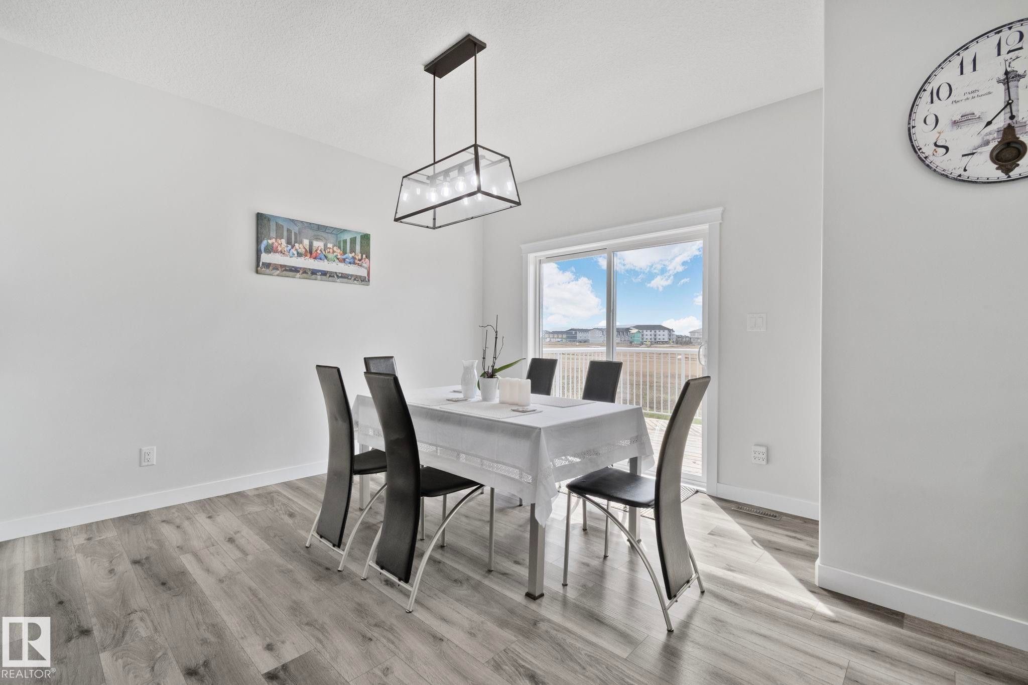 Spacious dining area featuring wood-finish flooring, a modern linear chandelier, and a sliding glass door providing exterior access - 334 Aston Close, Leduc, AB - Indoor Photo Showing Dining Room