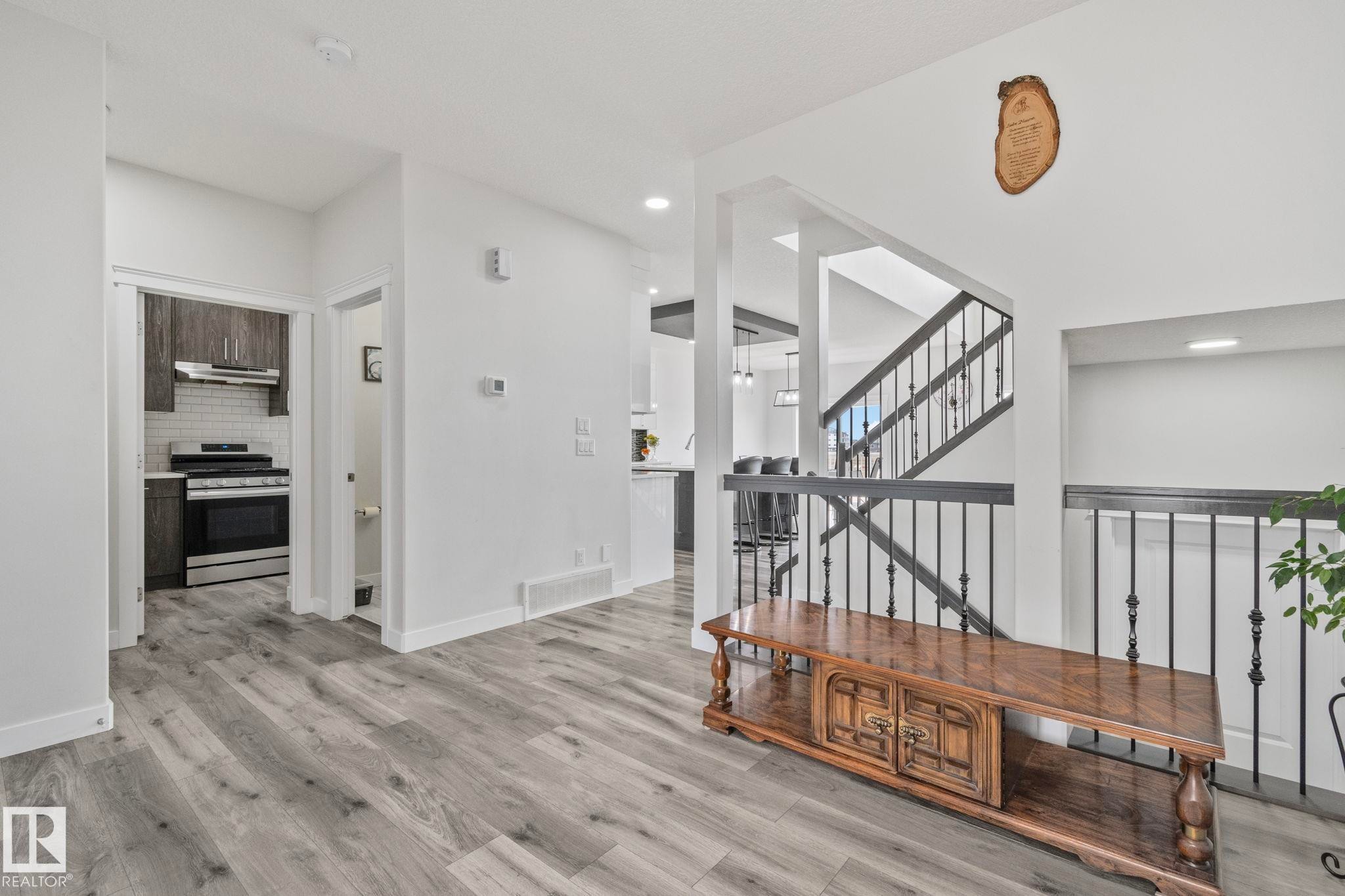 Spacious interior with wood-finish flooring, white walls, and a staircase featuring black wrought iron spindles - 334 Aston Close, Leduc, AB - Indoor Photo Showing Other Room