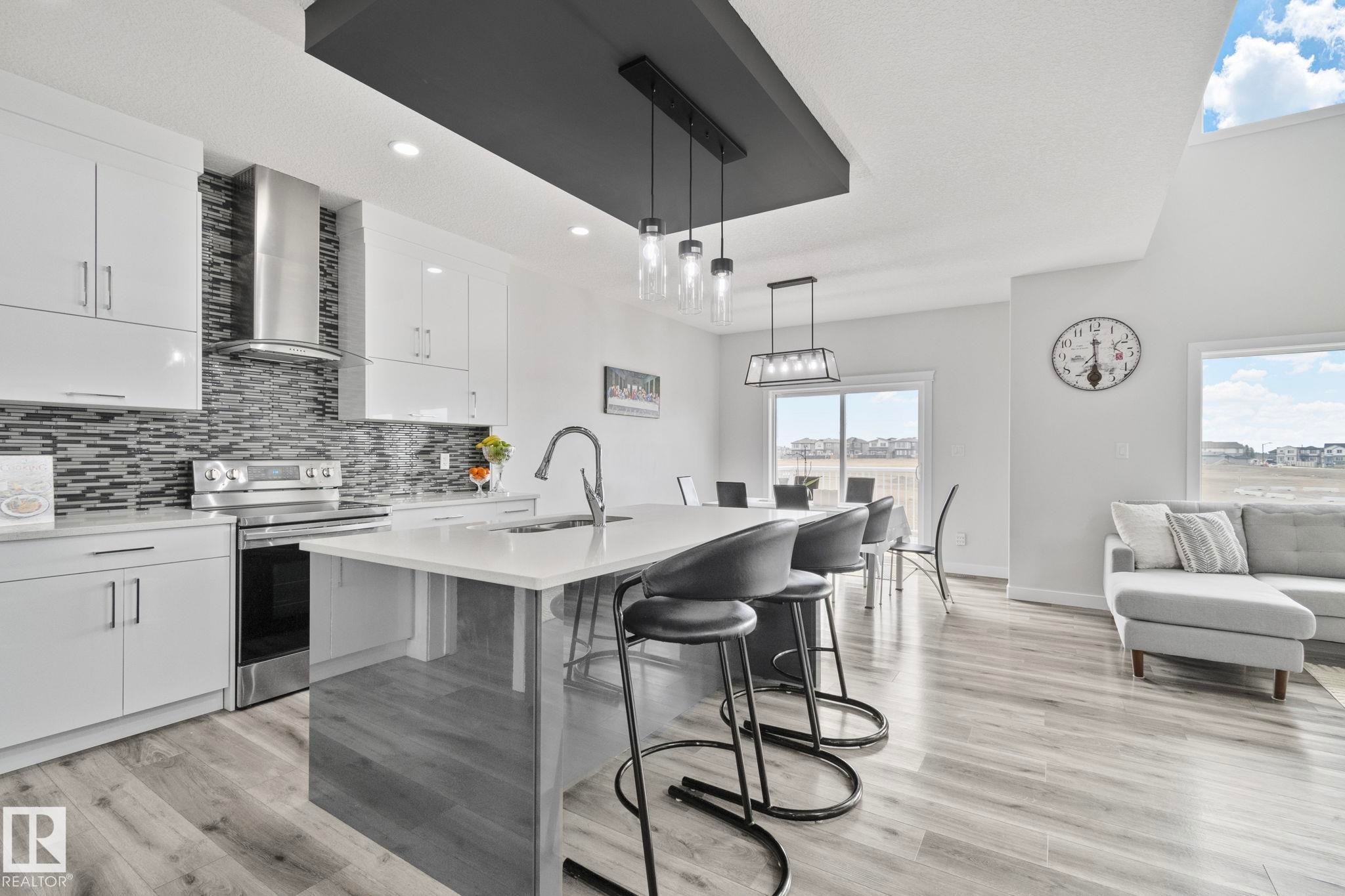 Modern kitchen featuring light cabinetry, stainless steel appliances, a mosaic tile backsplash, and a central island with a sink and seating - 334 Aston Close, Leduc, AB - Indoor Photo Showing Kitchen With Upgraded Kitchen
