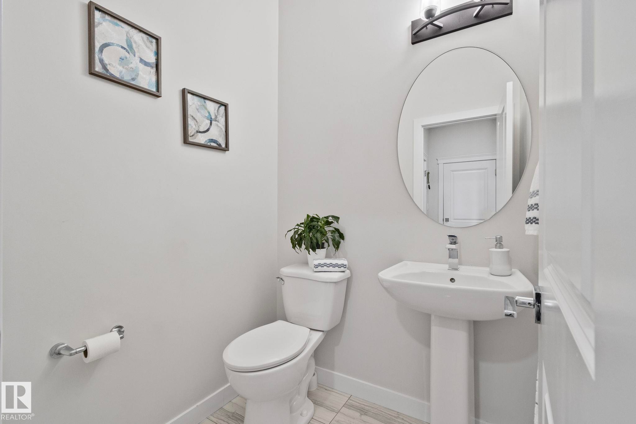 Bright powder room featuring a pedestal sink, oval vanity mirror, and contemporary wall sconce - 334 Aston Close, Leduc, AB - Indoor Photo Showing Bathroom