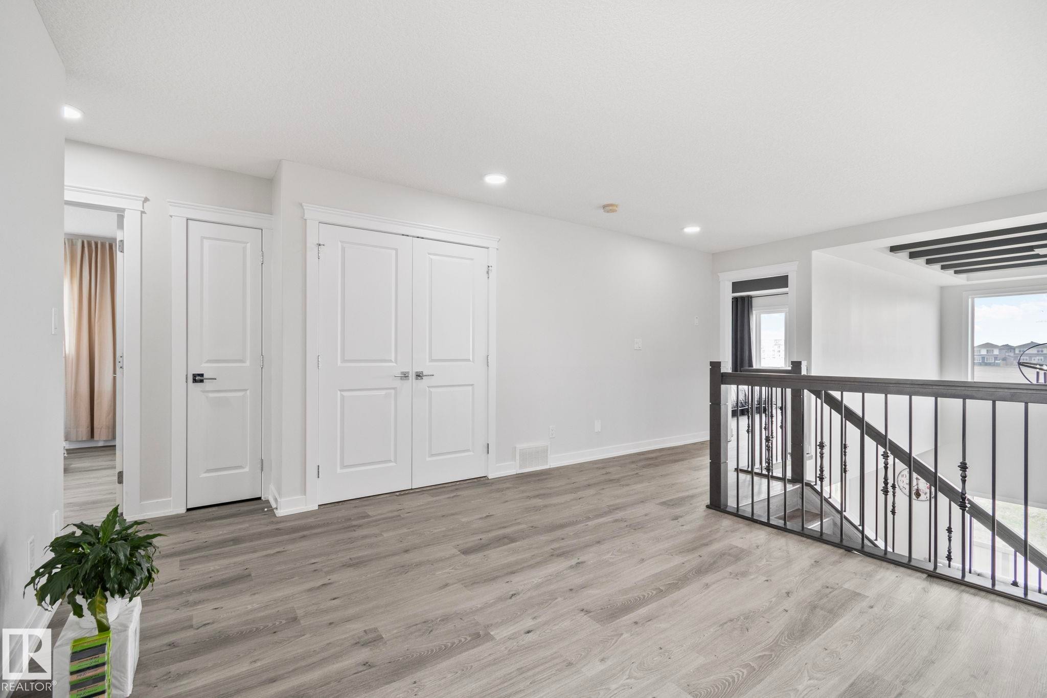 Spacious landing area featuring wood-finish flooring, recessed lighting, white trim, and a contemporary iron railing - 334 Aston Close, Leduc, AB - Indoor Photo Showing Other Room