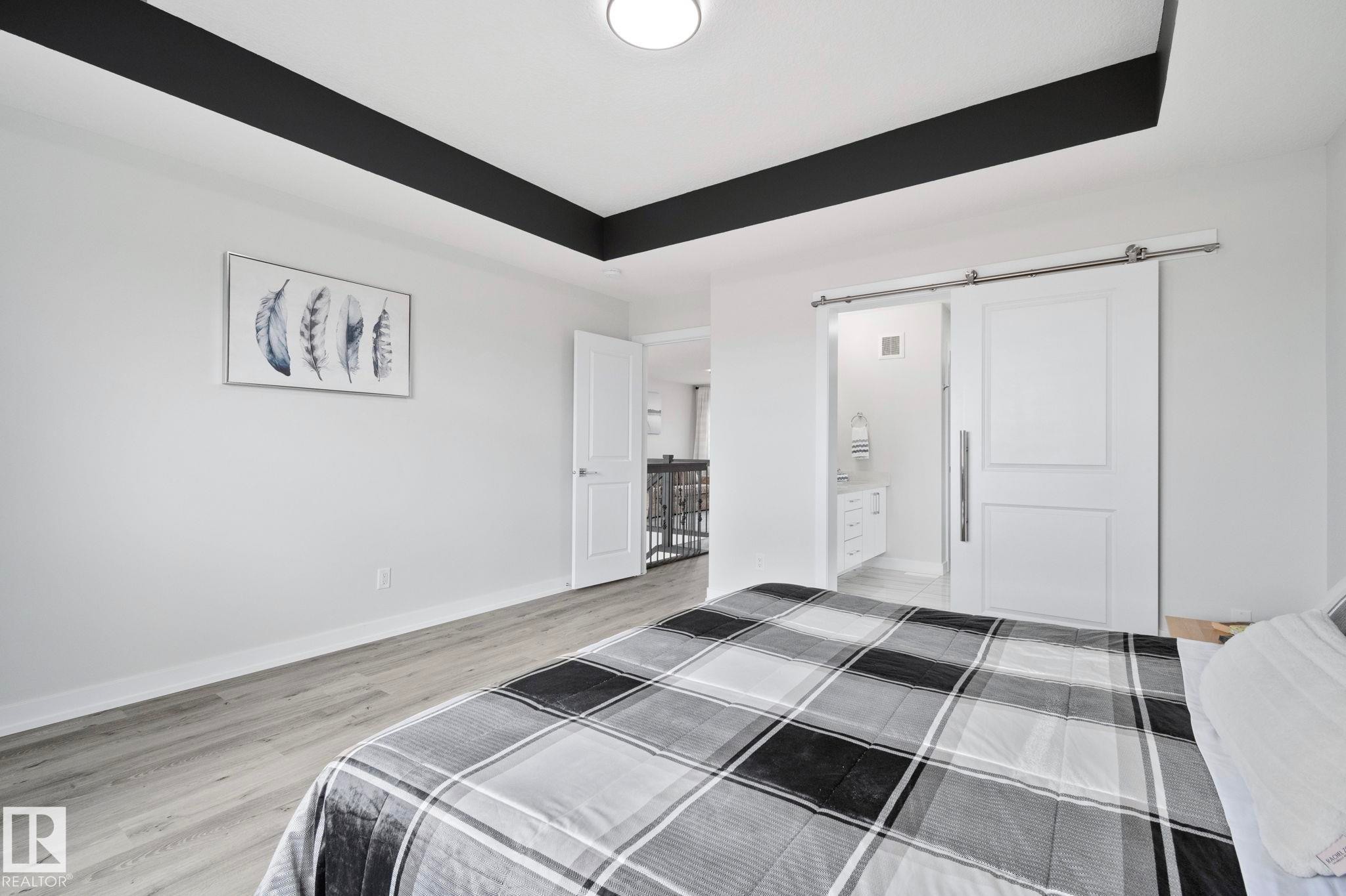 Spacious room featuring a tray ceiling with black accent, wood-finish flooring, and white walls - 334 Aston Close, Leduc, AB - Indoor