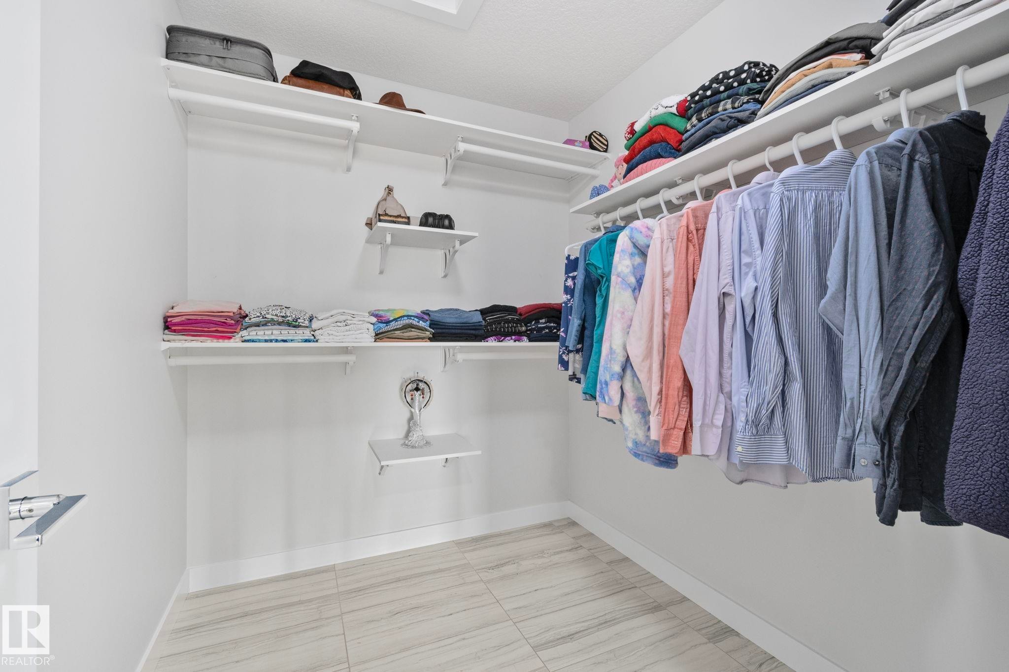 Walk-in closet featuring white wood-finish shelving, multiple hanging rods, and light-toned plank-style flooring - 334 Aston Close, Leduc, AB - Indoor With Storage