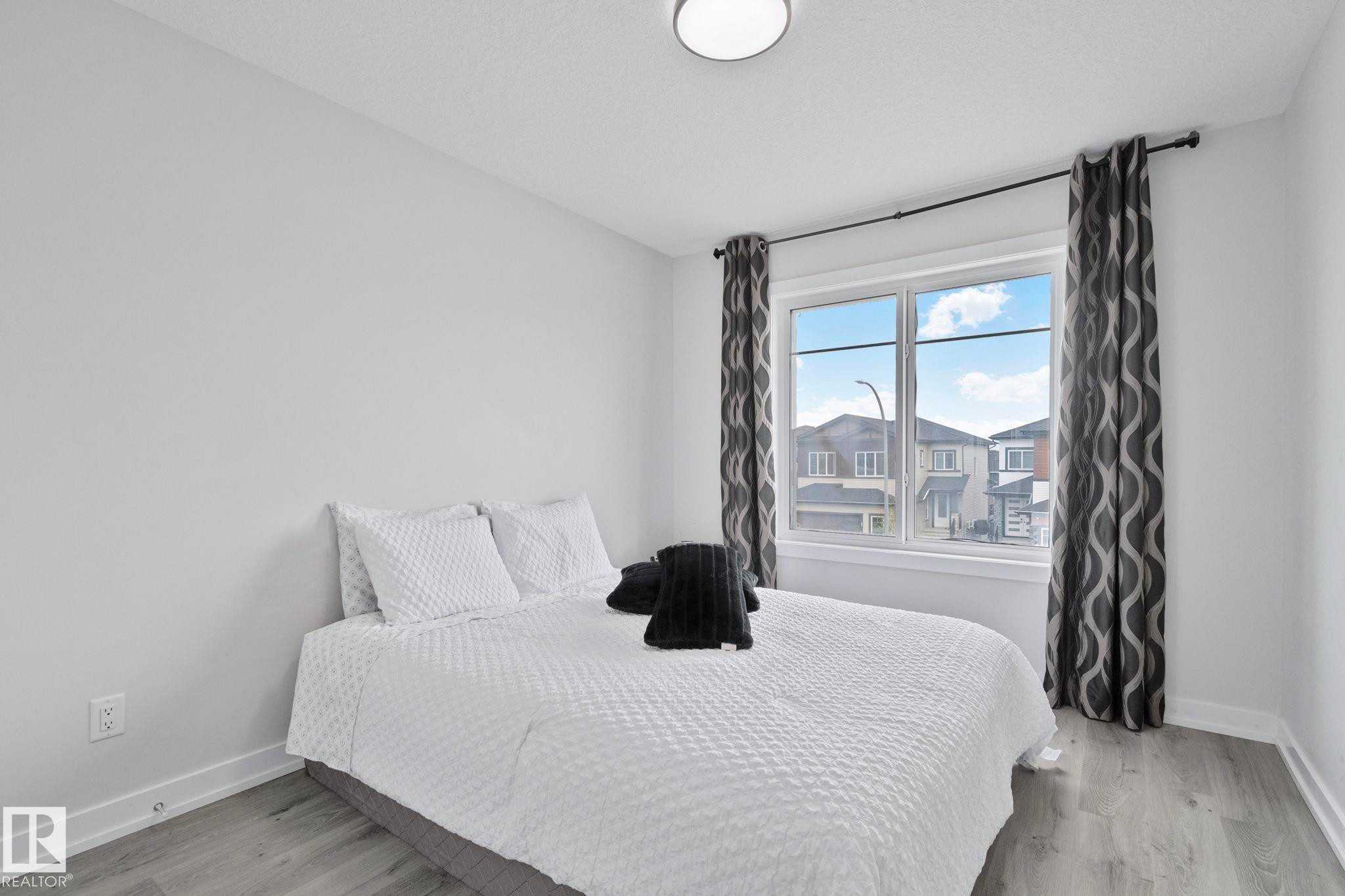 Bright room featuring a large window, light-toned walls, wood-finish flooring, and a flush mount ceiling light - 334 Aston Close, Leduc, AB - Indoor Photo Showing Bedroom