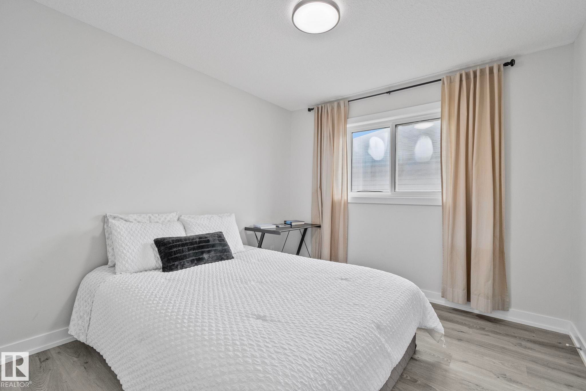 Bedroom featuring neutral wall paint, wood-finish flooring, a flush-mount ceiling light, and a window with curtains - 334 Aston Close, Leduc, AB - Indoor Photo Showing Bedroom