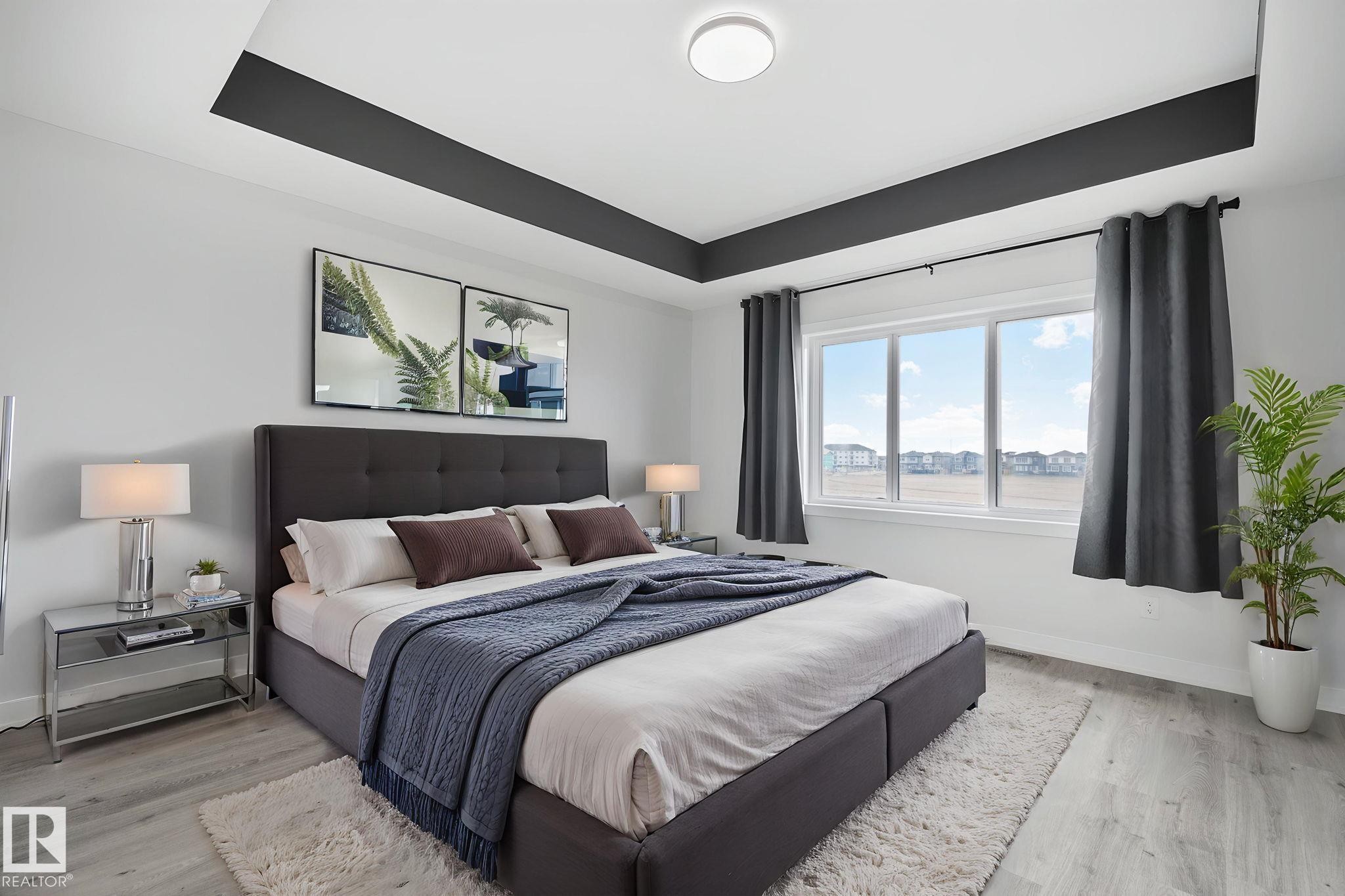 Recessed tray ceiling with contrasting accent, light wood-finish flooring, and large window with white trim - 334 Aston Close, Leduc, AB - Indoor Photo Showing Bedroom