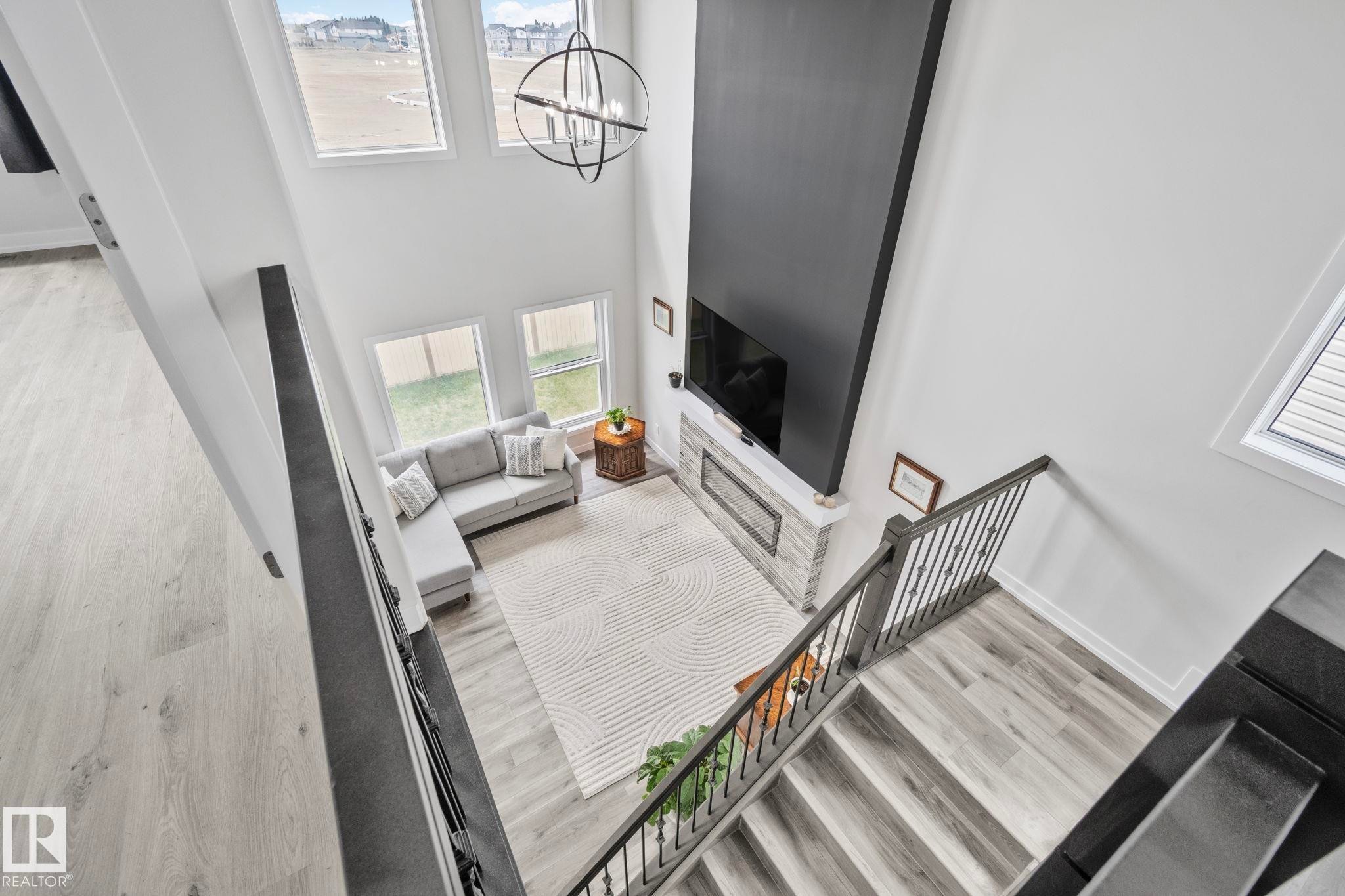 Two-story living area featuring a prominent dark accent wall, a fireplace with stone surround, high ceilings, multiple windows, and a modern circular chandelier - 334 Aston Close, Leduc, AB - Indoor Photo Showing Other Room
