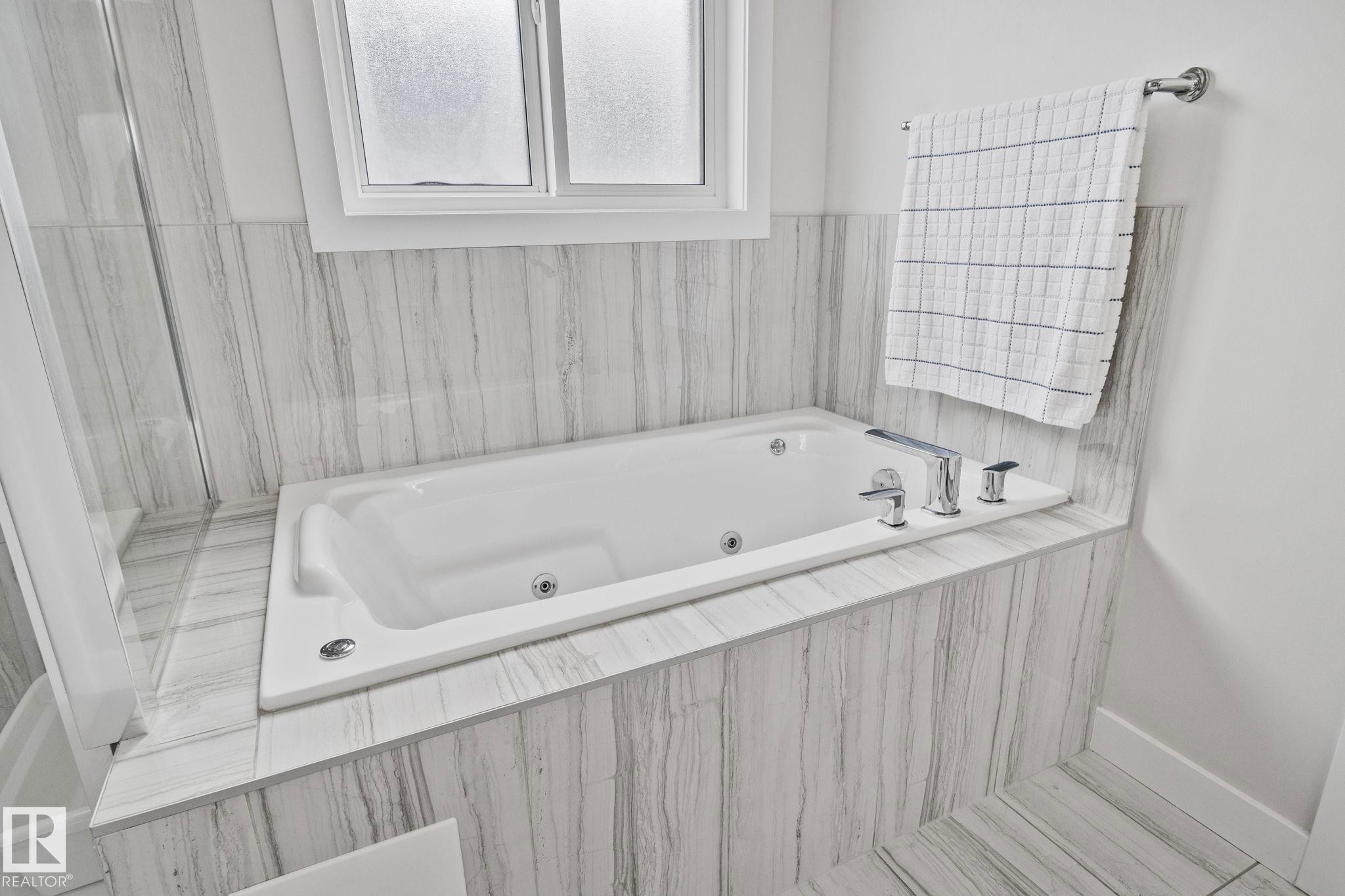 White soaking tub with integrated jets, chrome fixtures, and a frosted window - 334 Aston Close, Leduc, AB - Indoor Photo Showing Bathroom