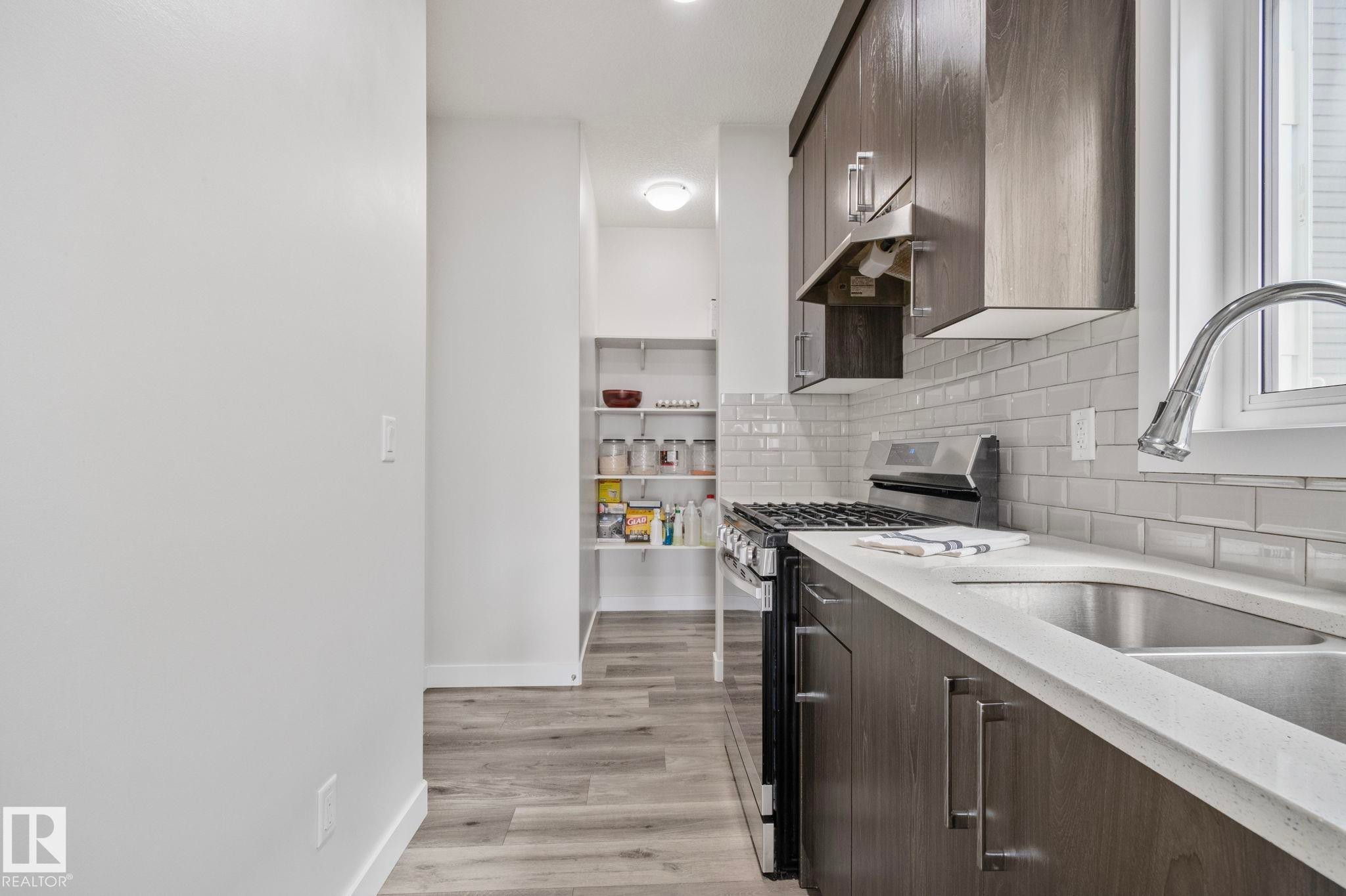 Modern kitchen featuring dark wood-finish cabinetry, light subway tile backsplash, white countertops, and stainless steel appliances - 334 Aston Close, Leduc, AB - Indoor Photo Showing Kitchen With Upgraded Kitchen