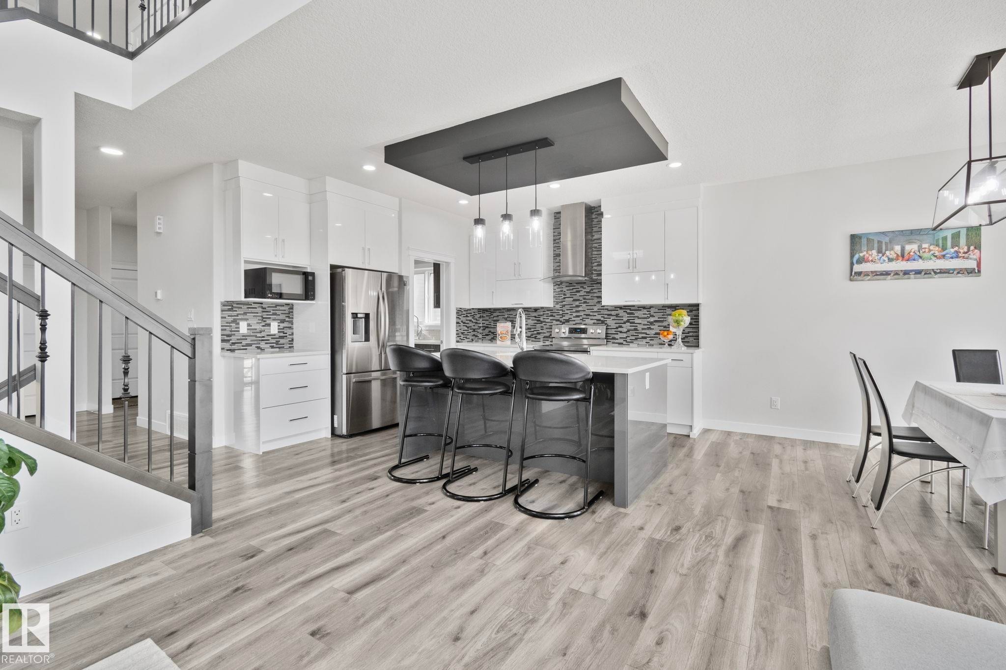 Gourmet kitchen featuring a central island with bar seating, stainless steel appliances, white cabinetry, and a mosaic tile backsplash - 334 Aston Close, Leduc, AB - Indoor