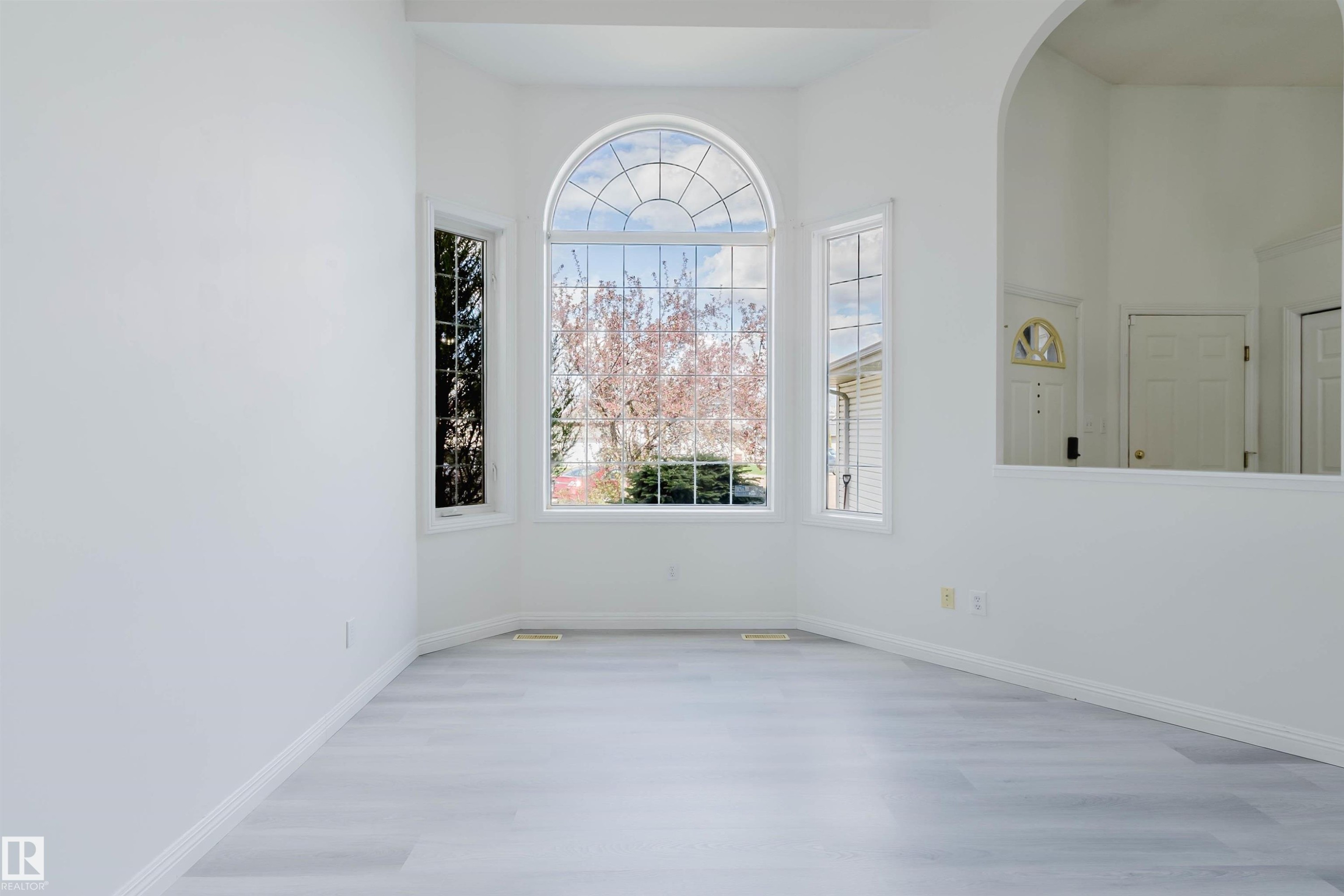 Bay window with arched transom, light wood-finish flooring, white baseboards, and an arched wall opening - 13755 131B Avenue, Edmonton, AB - Indoor Photo Showing Other Room