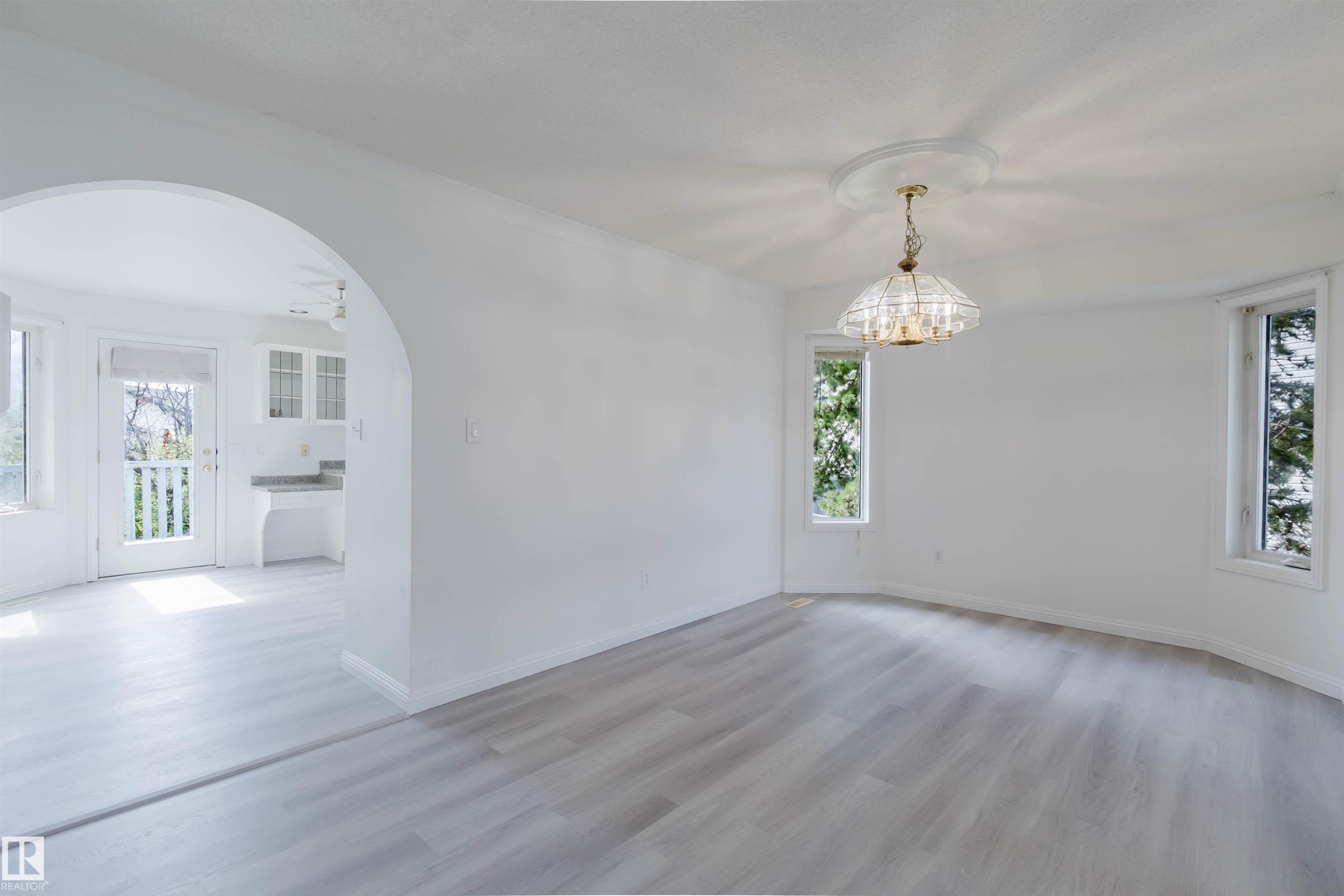 Spacious room featuring light wood-finish flooring, a decorative chandelier, and multiple windows providing natural light - 13755 131B Avenue, Edmonton, AB - Indoor Photo Showing Other Room