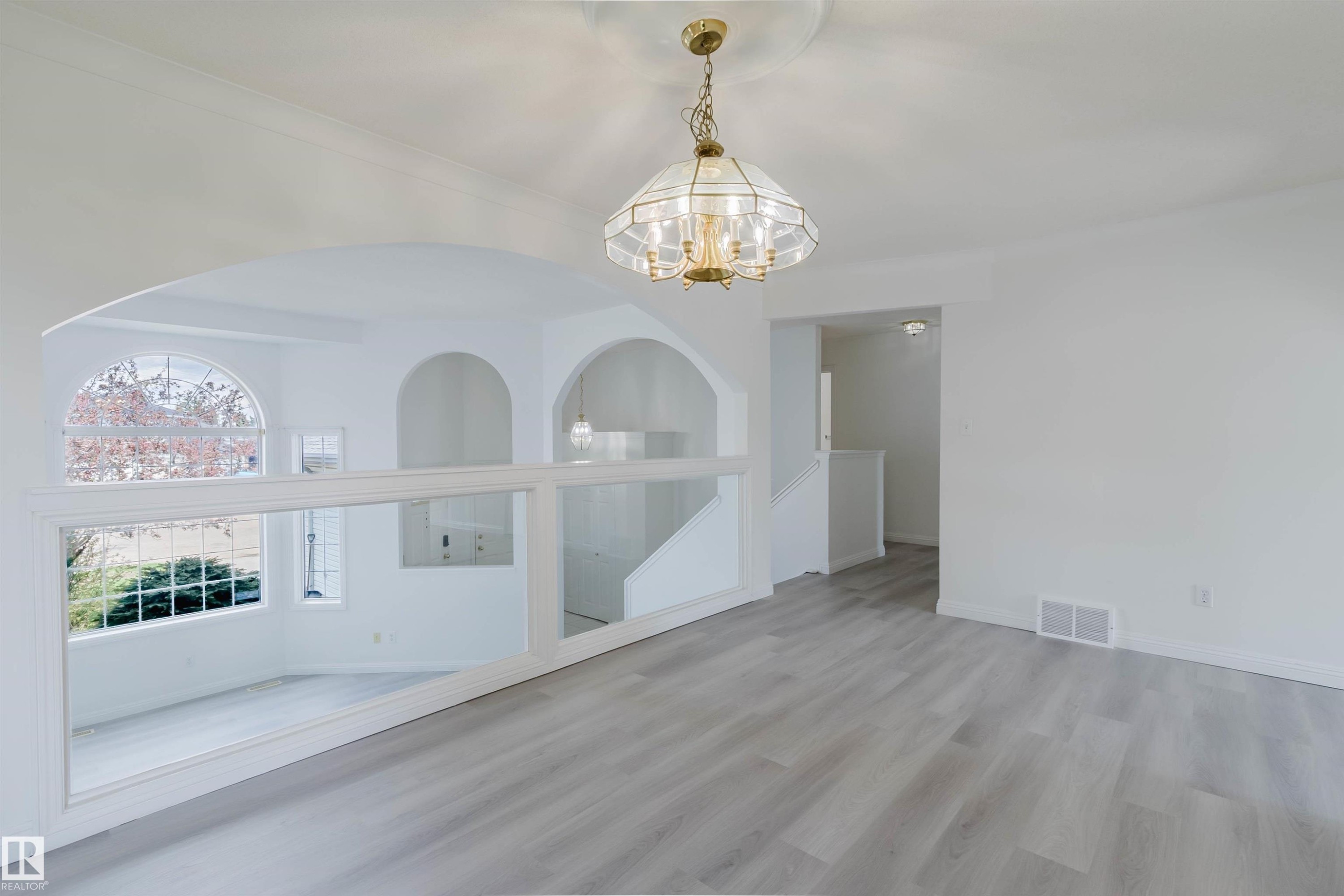 Spacious interior featuring light wood-finish flooring, a decorative chandelier with a ceiling medallion, and arched architectural openings - 13755 131B Avenue, Edmonton, AB - Indoor Photo Showing Other Room