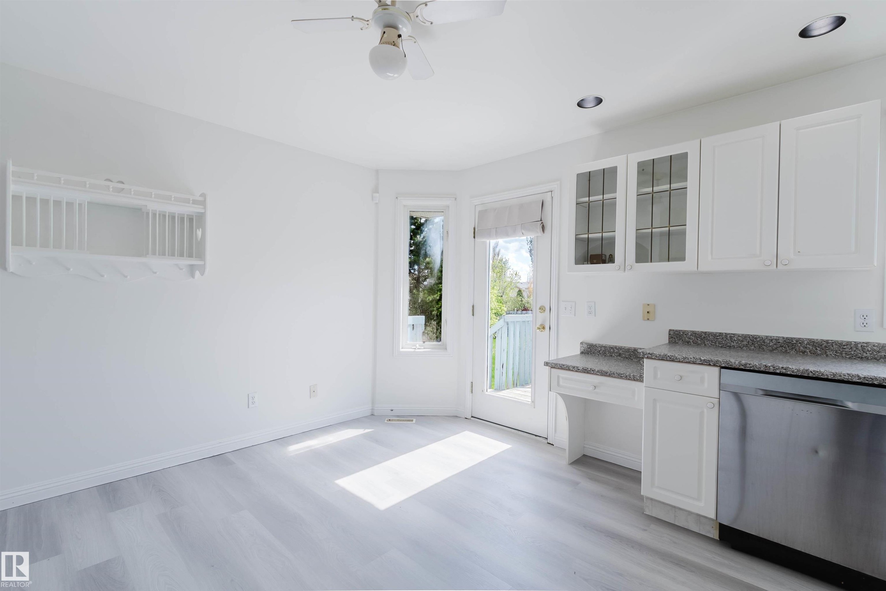Kitchen area featuring white cabinetry with some glass-front doors, a stainless steel dishwasher, and a speckled countertop - 13755 131B Avenue, Edmonton, AB - Indoor