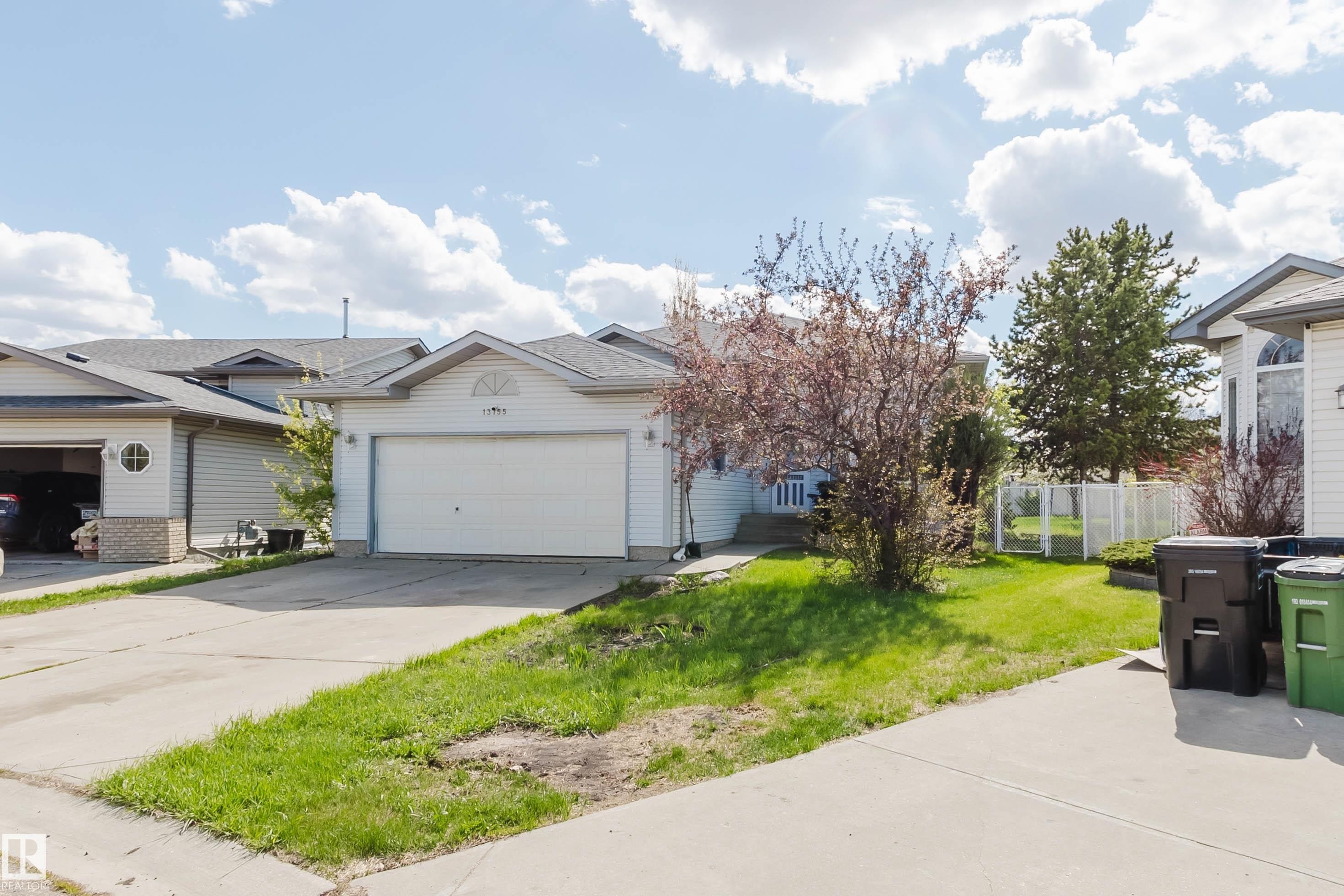 Exterior featuring light-colored siding, an attached garage, a mature front yard tree, and a concrete driveway - 13755 131B Avenue, Edmonton, AB - Outdoor