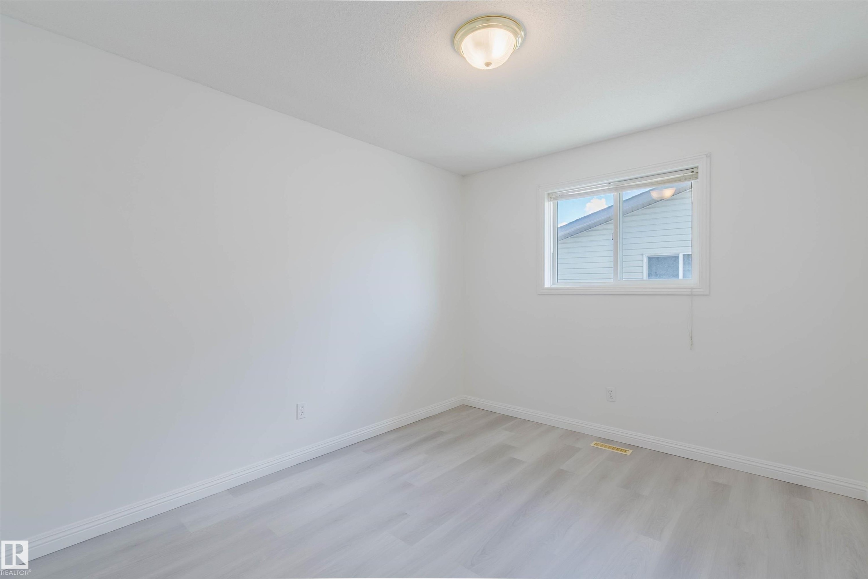 Bright room featuring wood-finish flooring, white baseboards, a single window, and a flush-mount ceiling light fixture - 13755 131B Avenue, Edmonton, AB - Indoor Photo Showing Other Room