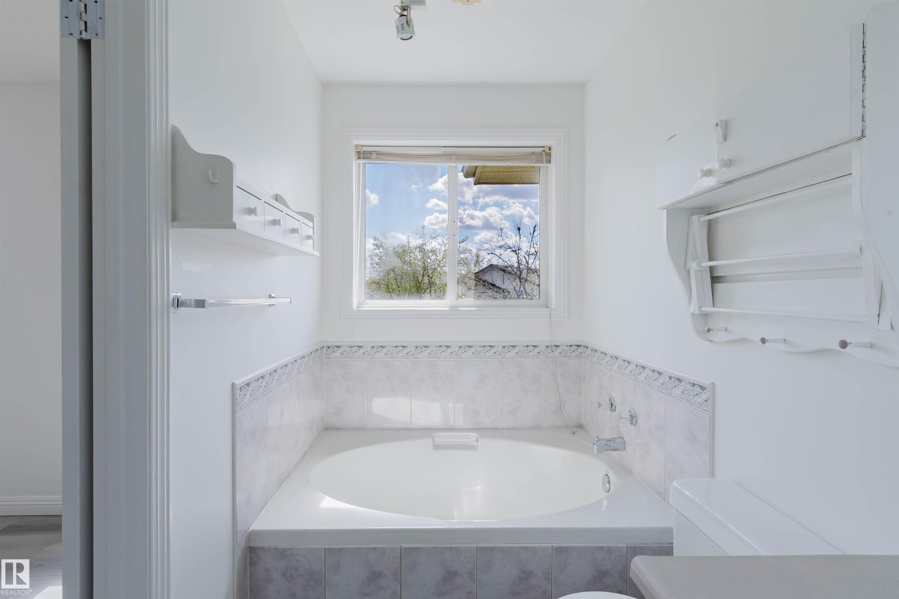Built-in soaking tub with tile surround, framed by a window providing natural light - 13755 131B Avenue, Edmonton, AB - Indoor Photo Showing Bathroom