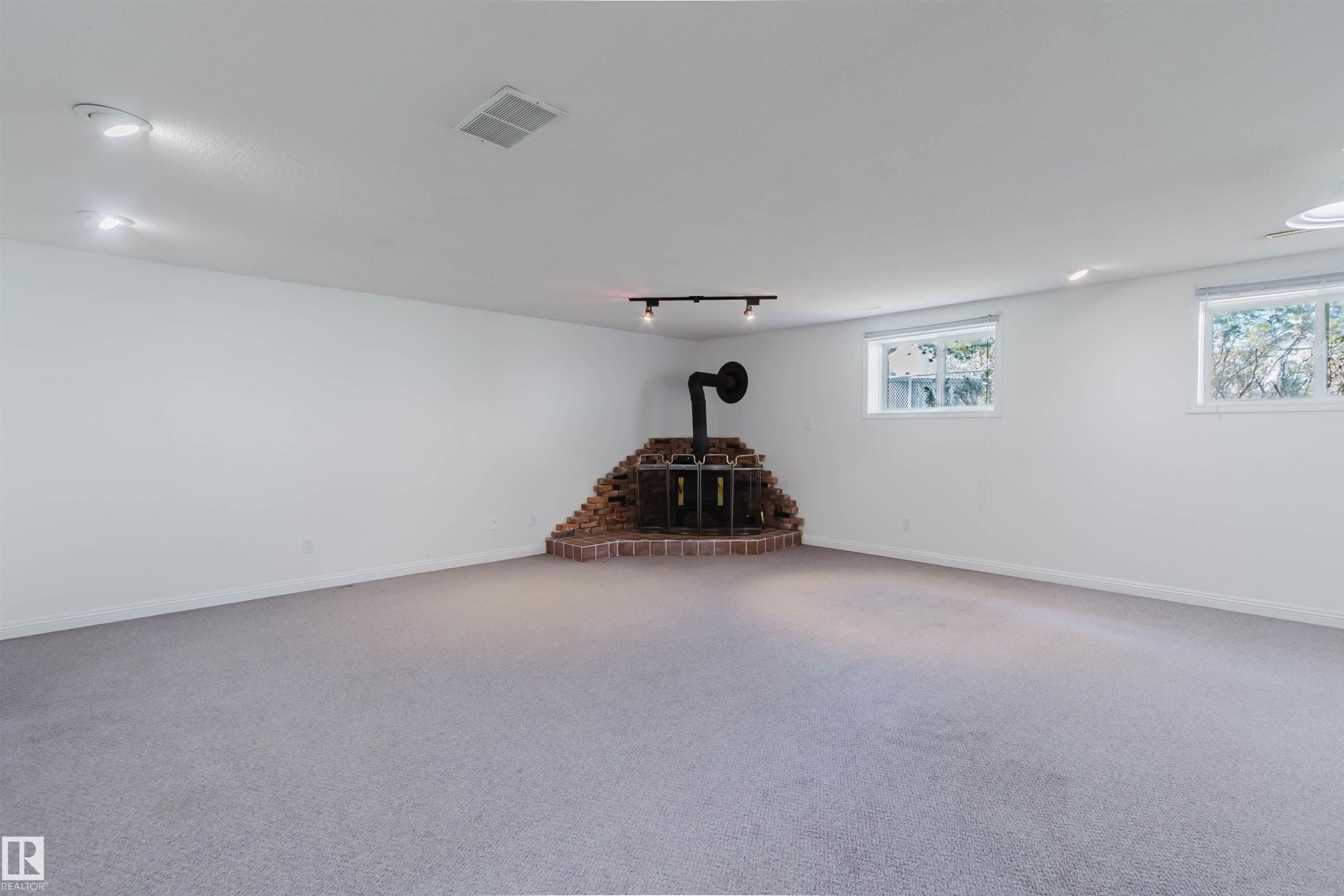 Spacious room featuring light gray carpeting, crisp white walls, multiple windows providing natural light, recessed lighting, and a corner brick-base stove - 13755 131B Avenue, Edmonton, AB - Indoor